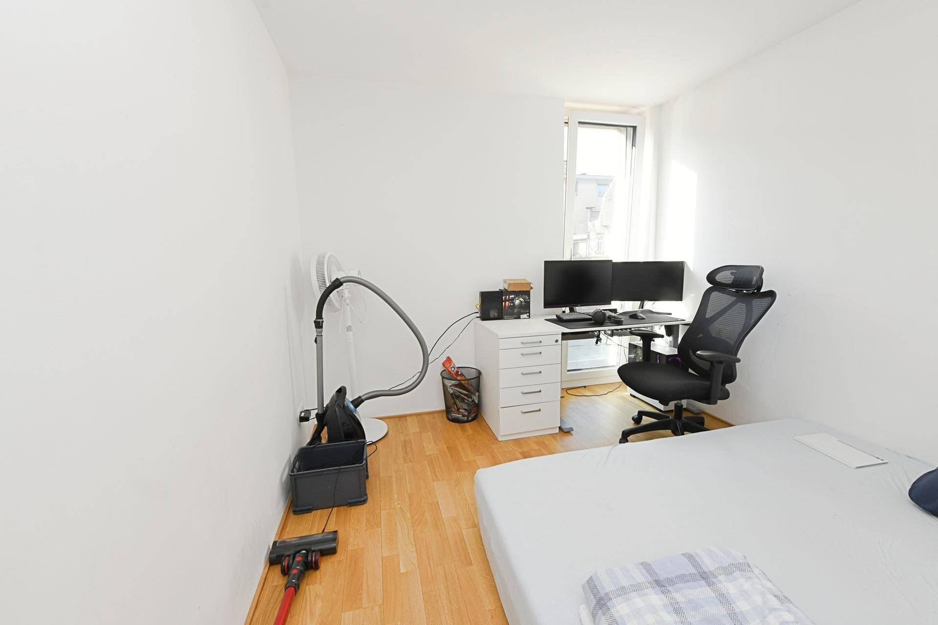 Schlafzimmer mit Holzboden, Schreibtisch und großem Fenster für viel Tageslicht.