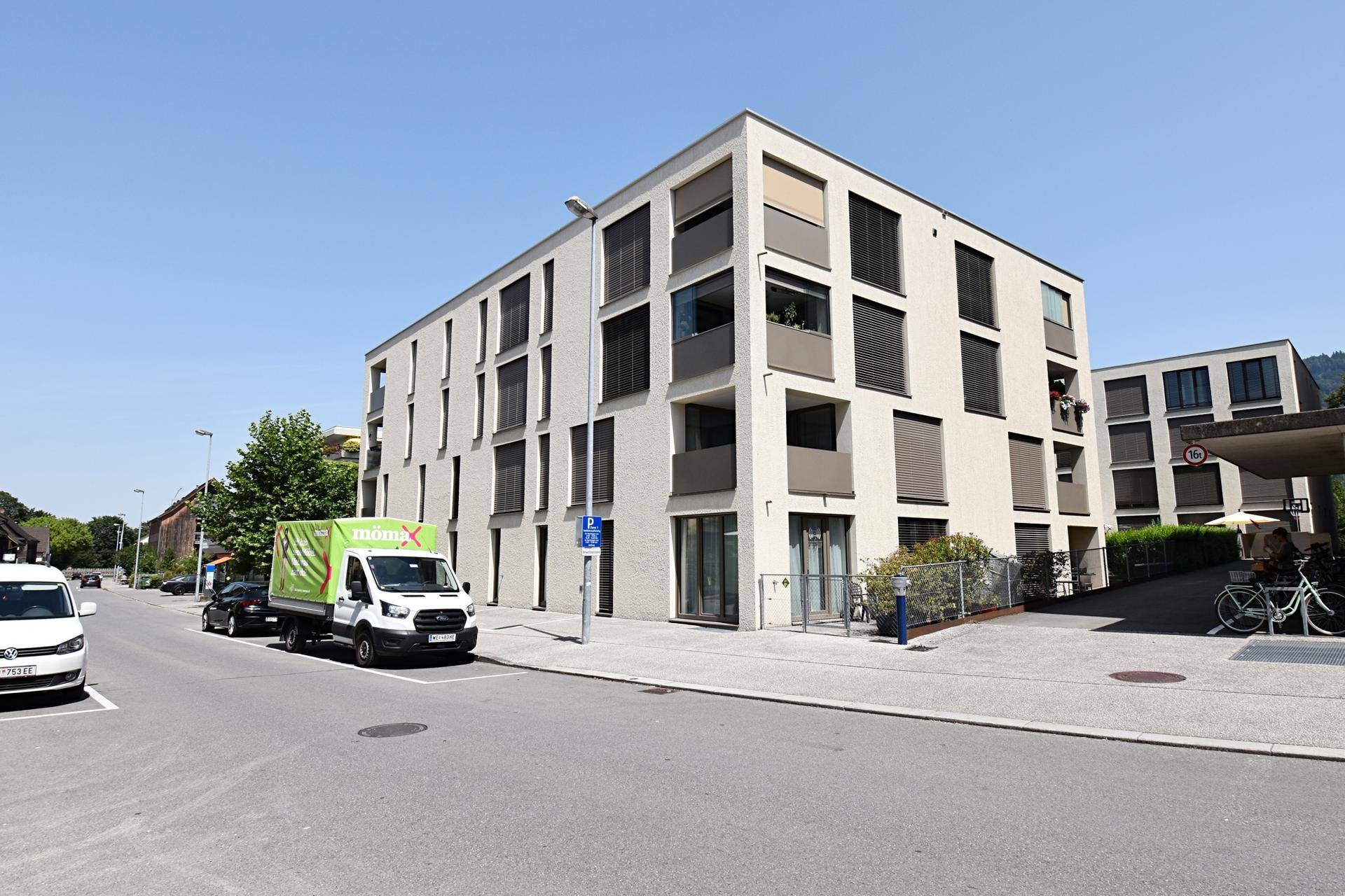Modernes Mehrfamilienhaus mit Balkonen und großen Fenstern an einer Straße.