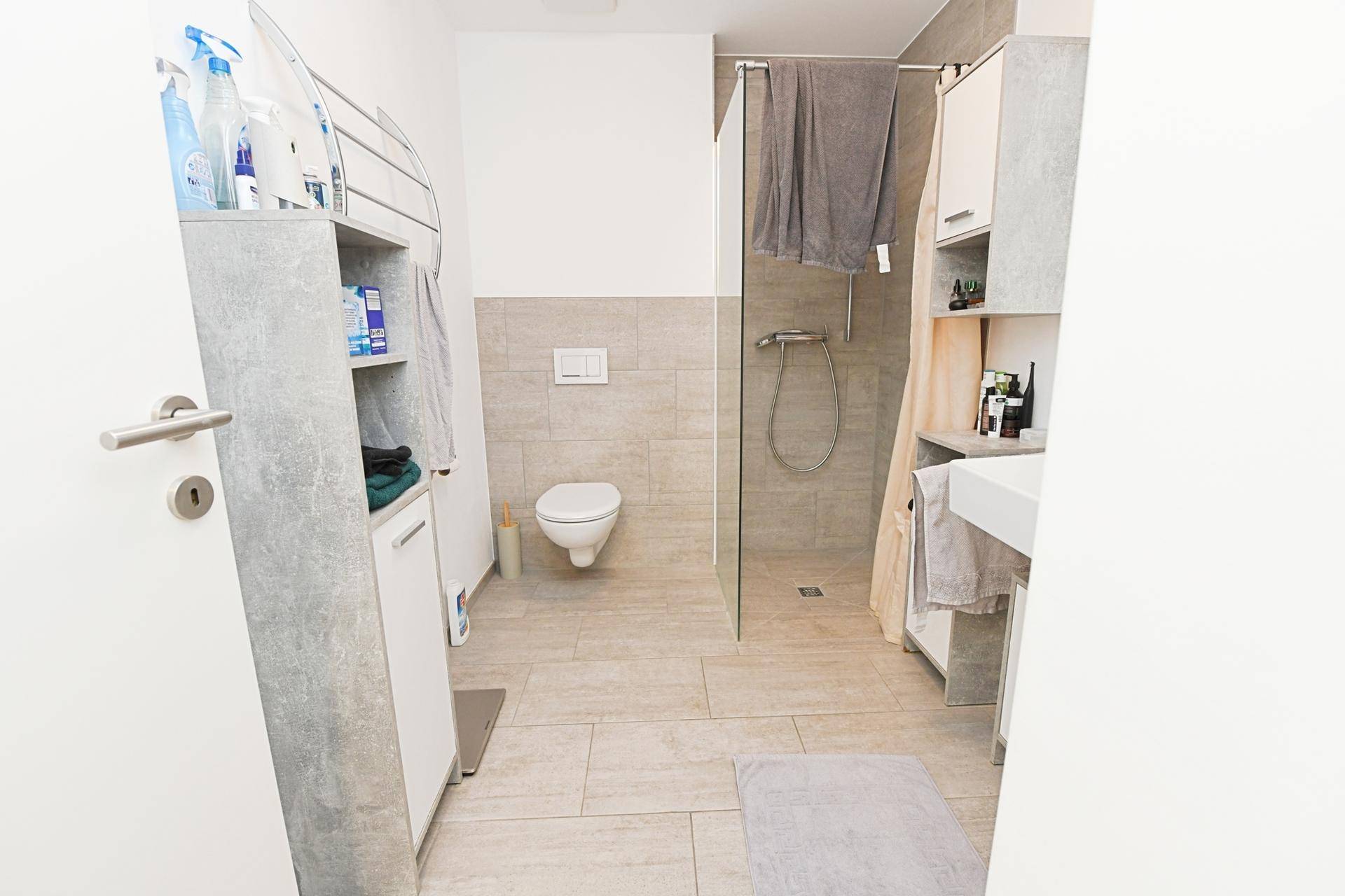 Modernes Badezimmer mit begehbarer Dusche, Wand-WC und hellen Fliesen.