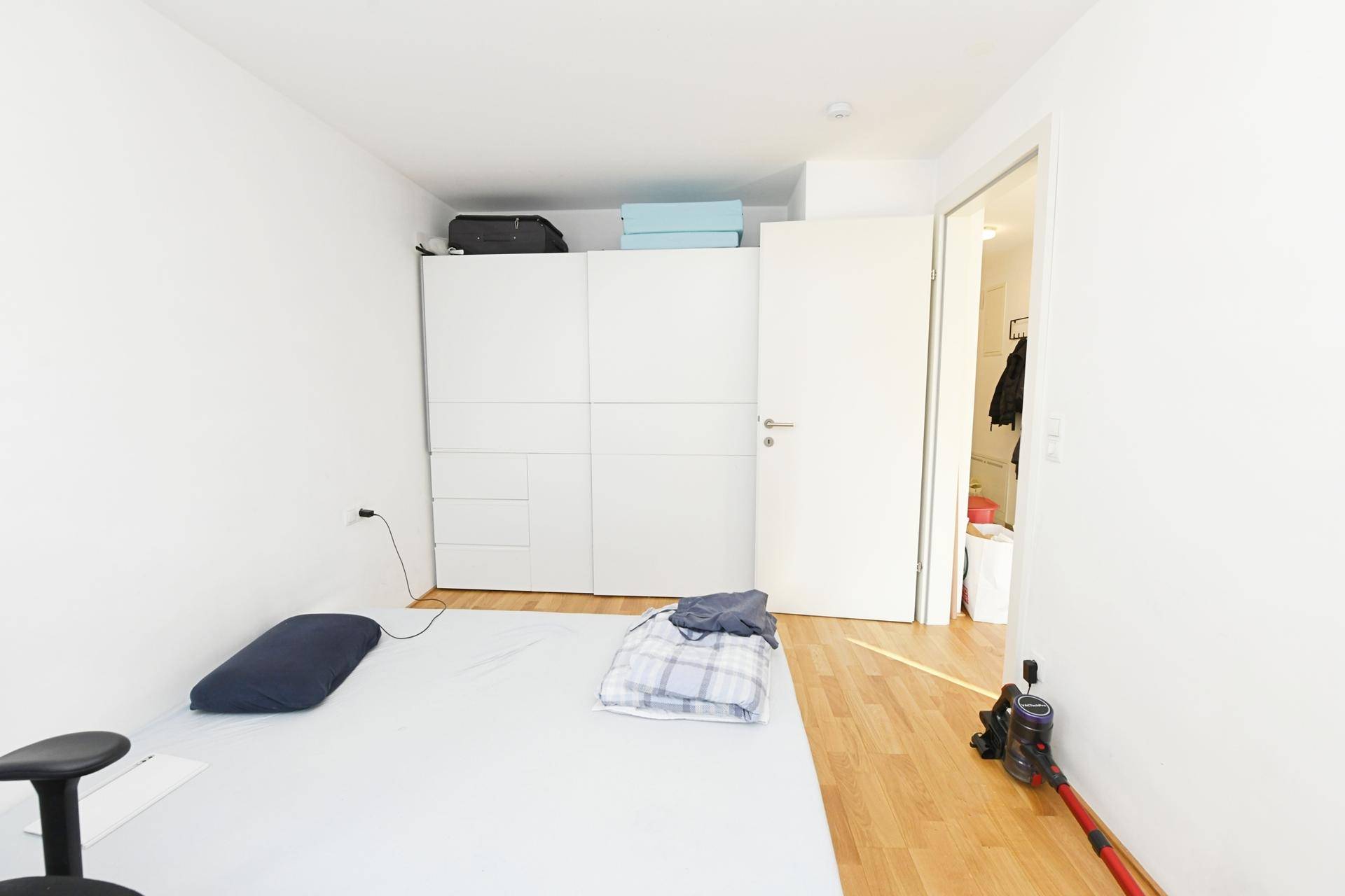 Schlafzimmer mit Holzboden, weißem Kleiderschrank und Zugang zu einem weiteren Raum.