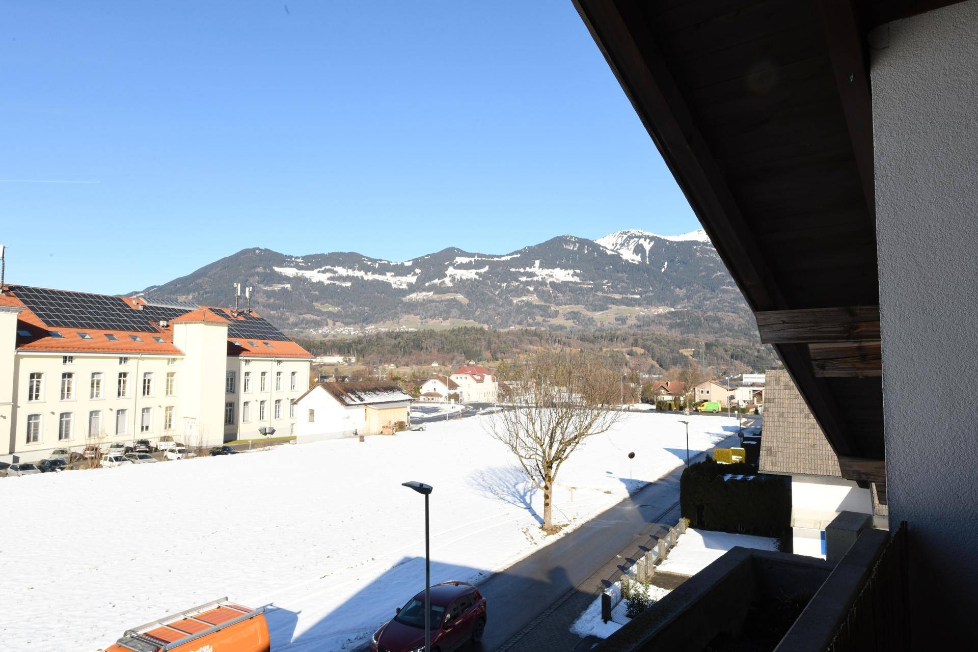 Weitblick vom Balkon über verschneite Felder und Berge an einem sonnigen Tag.