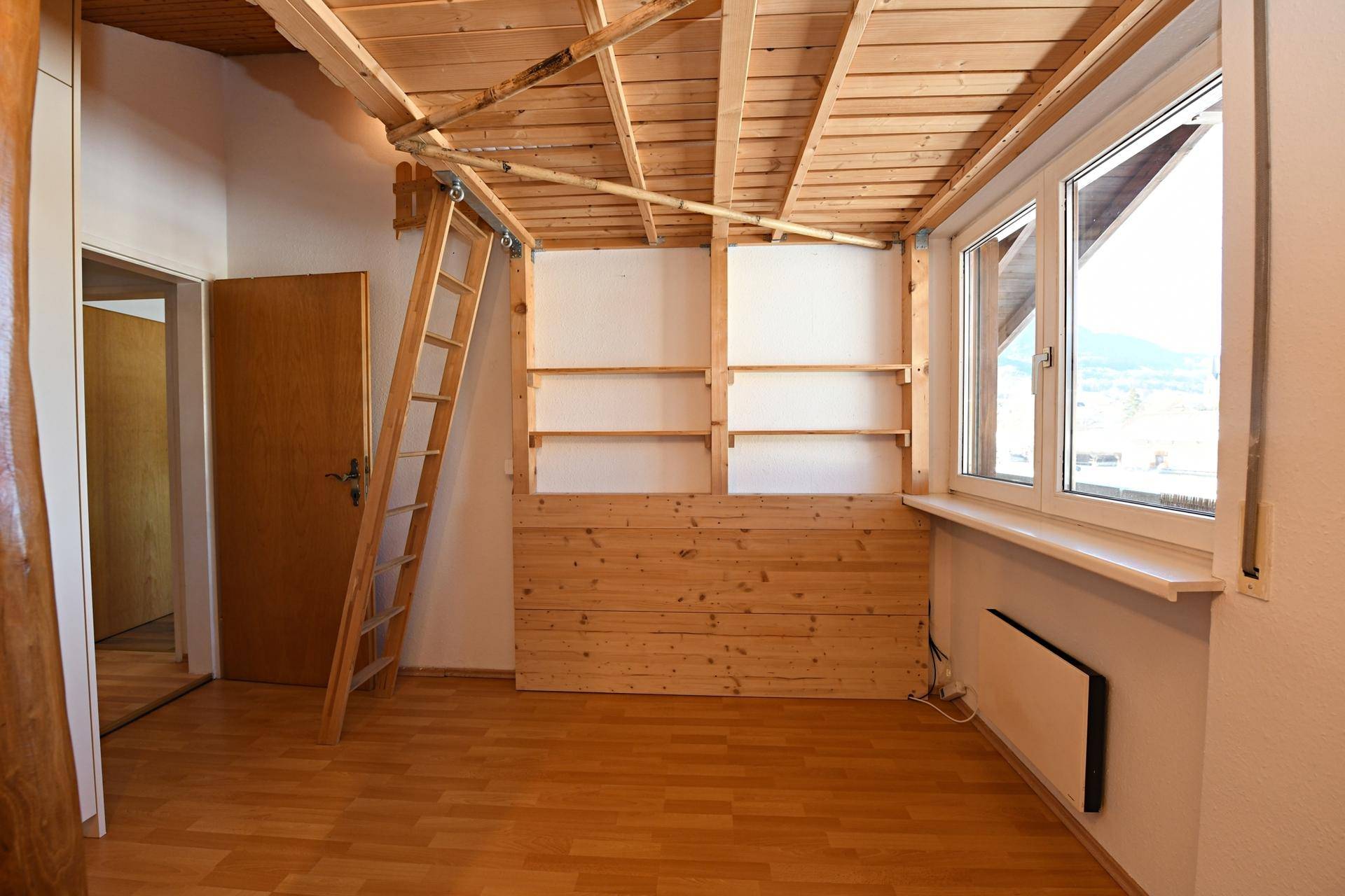 Helles Zimmer mit Holzboden, Holzdecke und Fenster mit Blick nach draußen.
