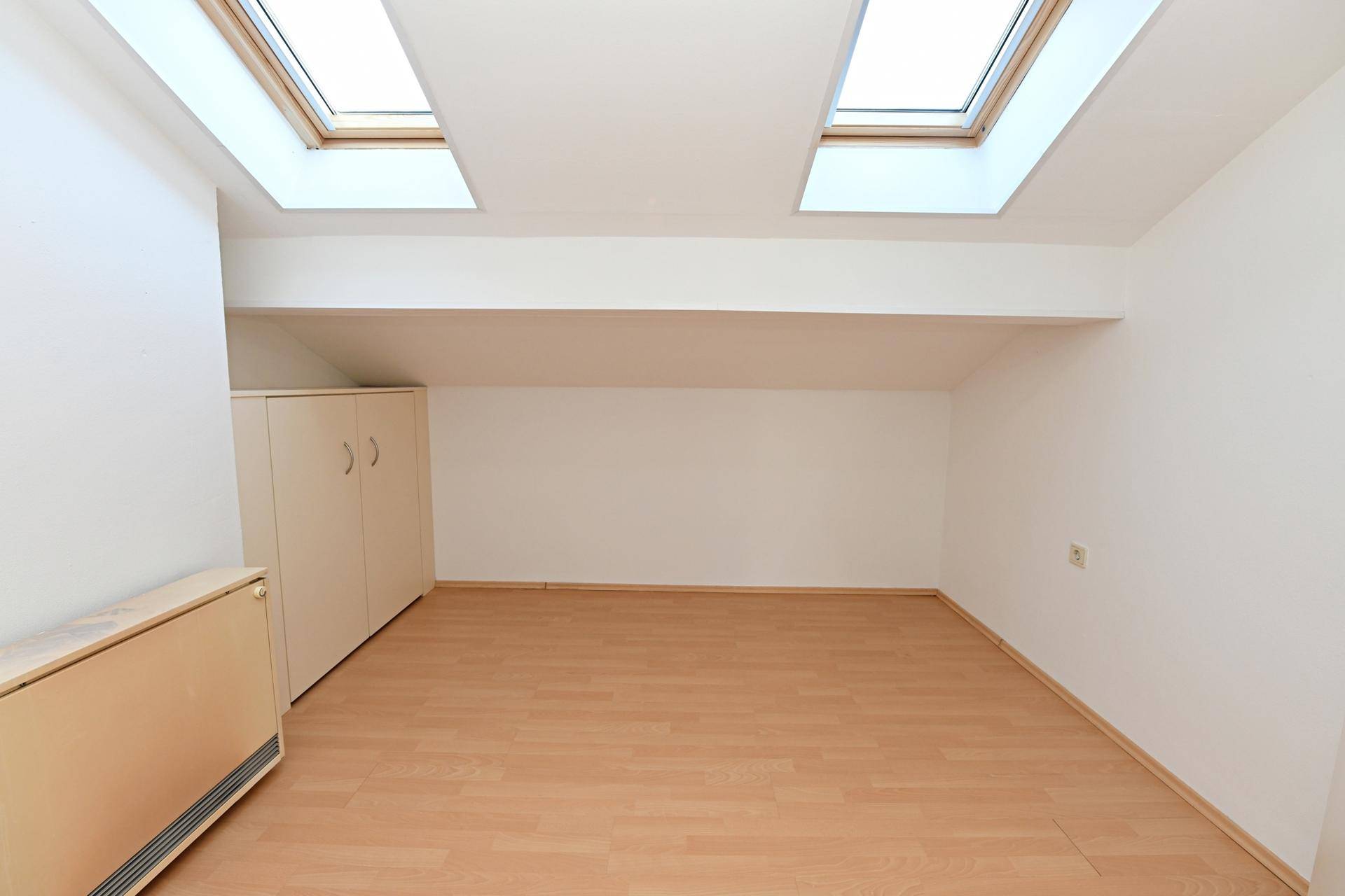 Helles Zimmer mit Laminatboden, Dachschrägen und zwei Dachfenstern für natürliche Belichtung.