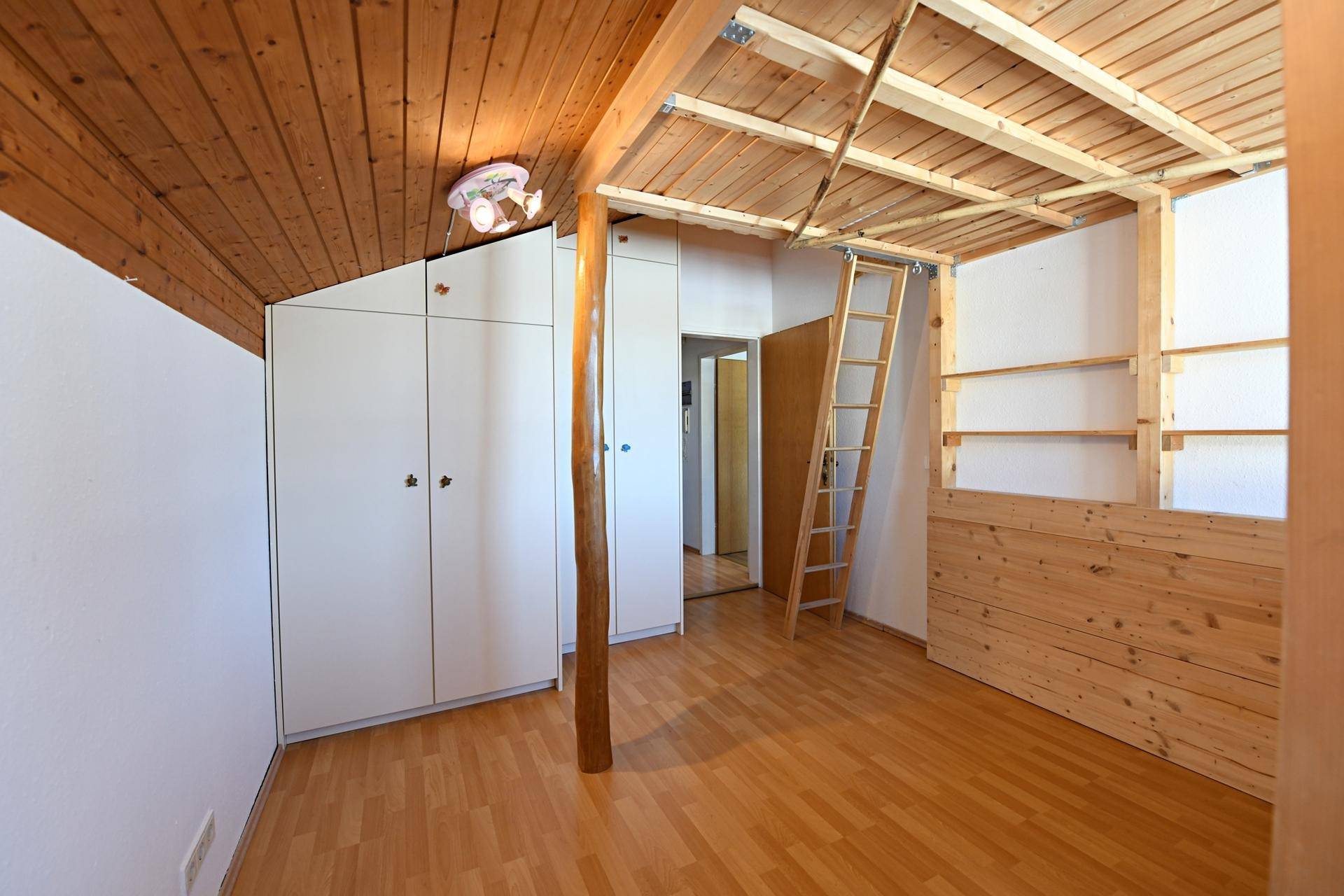 Gemütliches Zimmer mit Holzboden, Holzdecke und einer Holzleiter zu einem Hochbett.