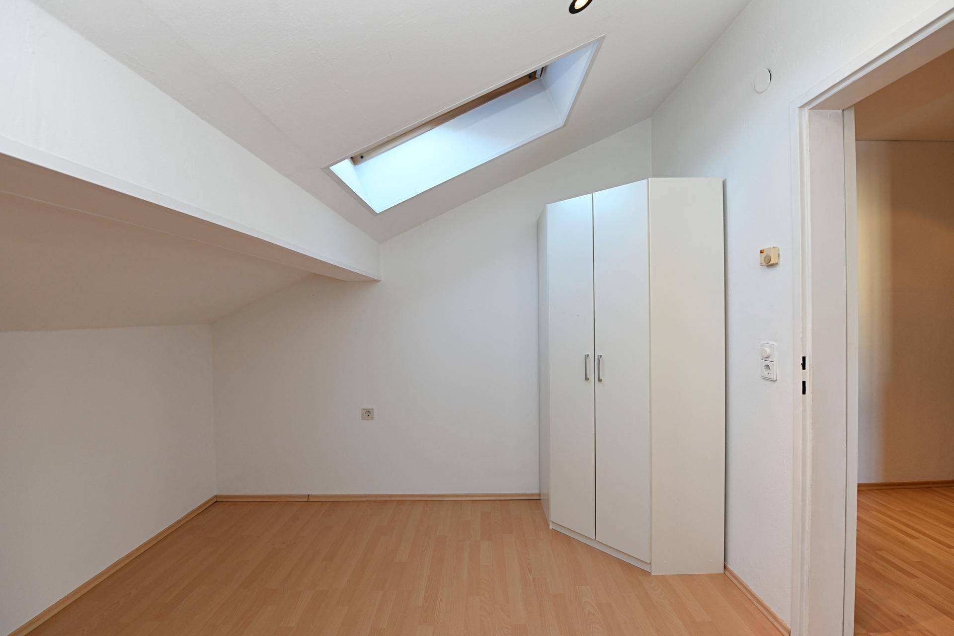Freundliches Zimmer mit Laminatboden, Dachschräge und einem Dachfenster für angenehmes Licht.