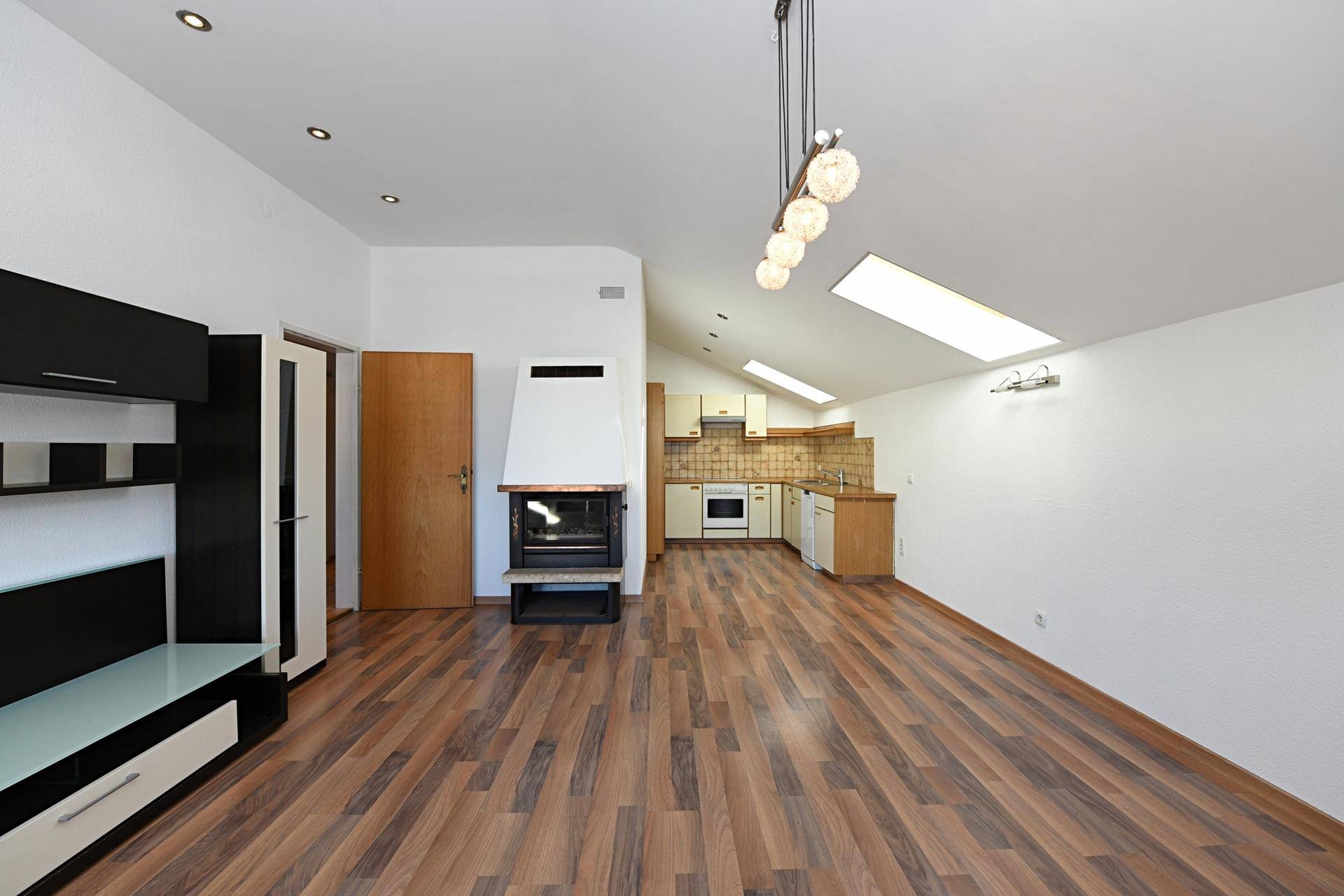 Geräumiger Wohnbereich mit Laminatboden, Kamin und integrierter Küche unter Dachschrägen.