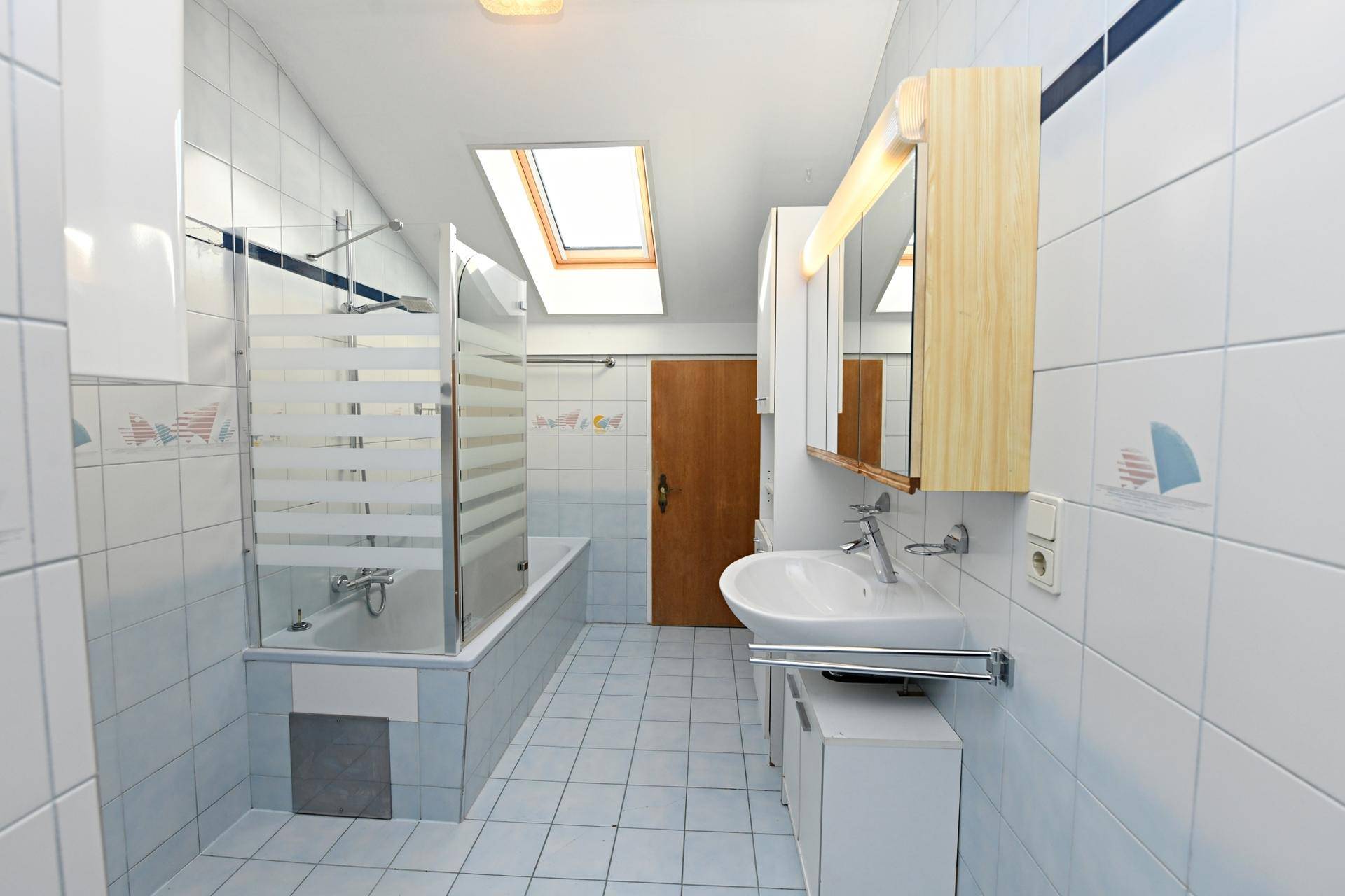 Badezimmer mit hellblauen Fliesen, Badewanne mit Duschabtrennung und Dachfenster.
