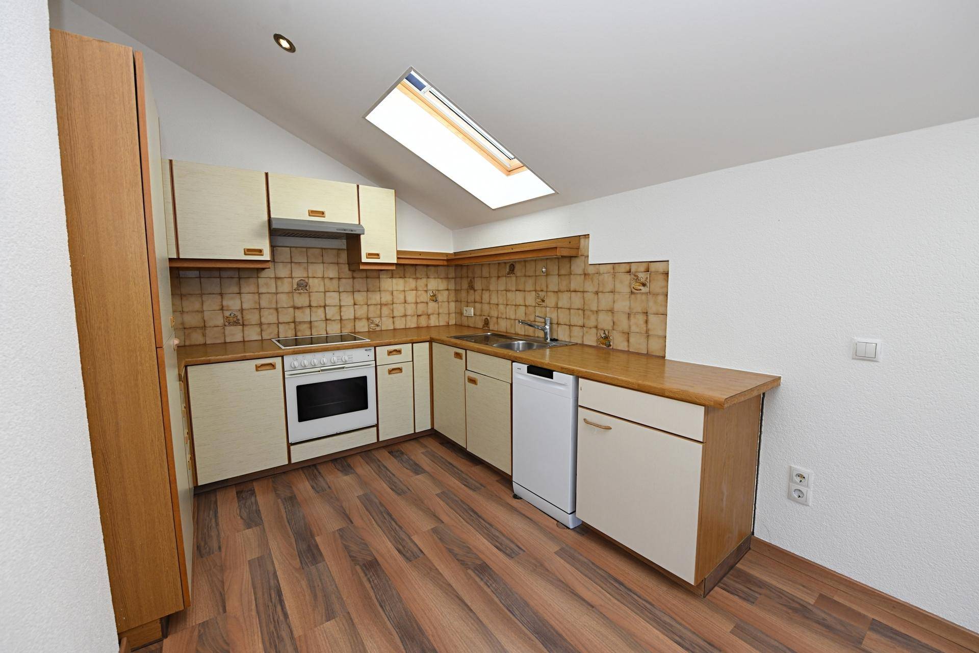Funktionale Küche mit hellen Schränken, Fliesenrückwand und Dachfenster für Tageslicht.