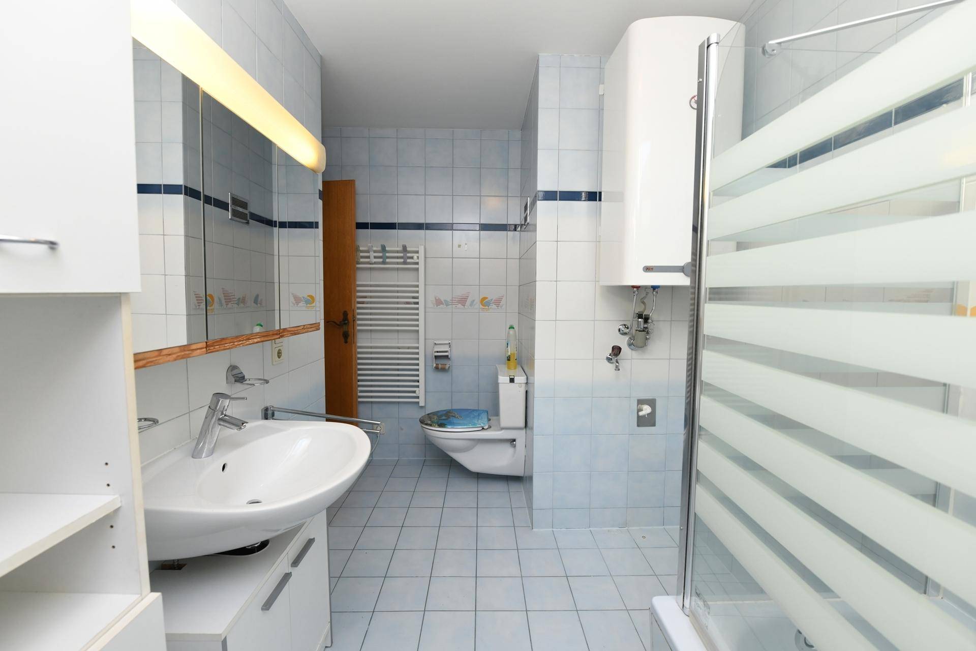 Badezimmer mit WC, Dusche, Waschbecken und hellblauen Fliesen.