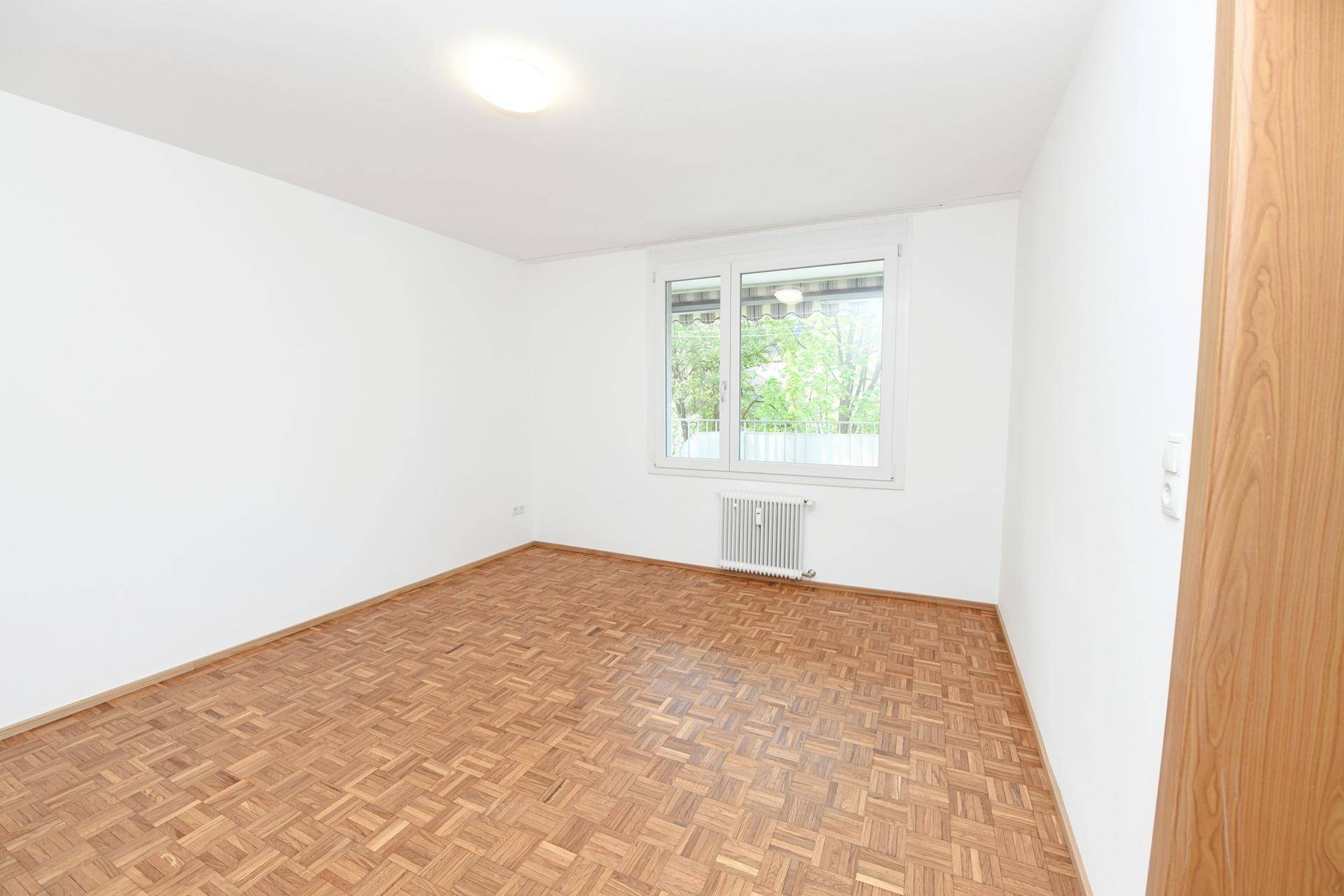 Helles Schlafzimmer mit Parkettboden und Fenster, ideal für Ruhe und Entspannung.