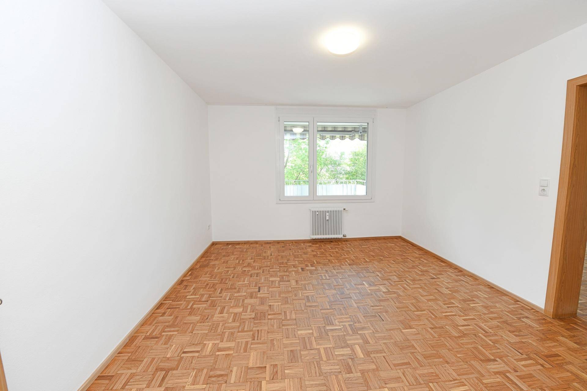 Leeres Schlafzimmer mit Parkettboden und Fenster, bietet eine neutrale Basis für persönliche Einrichtung.
