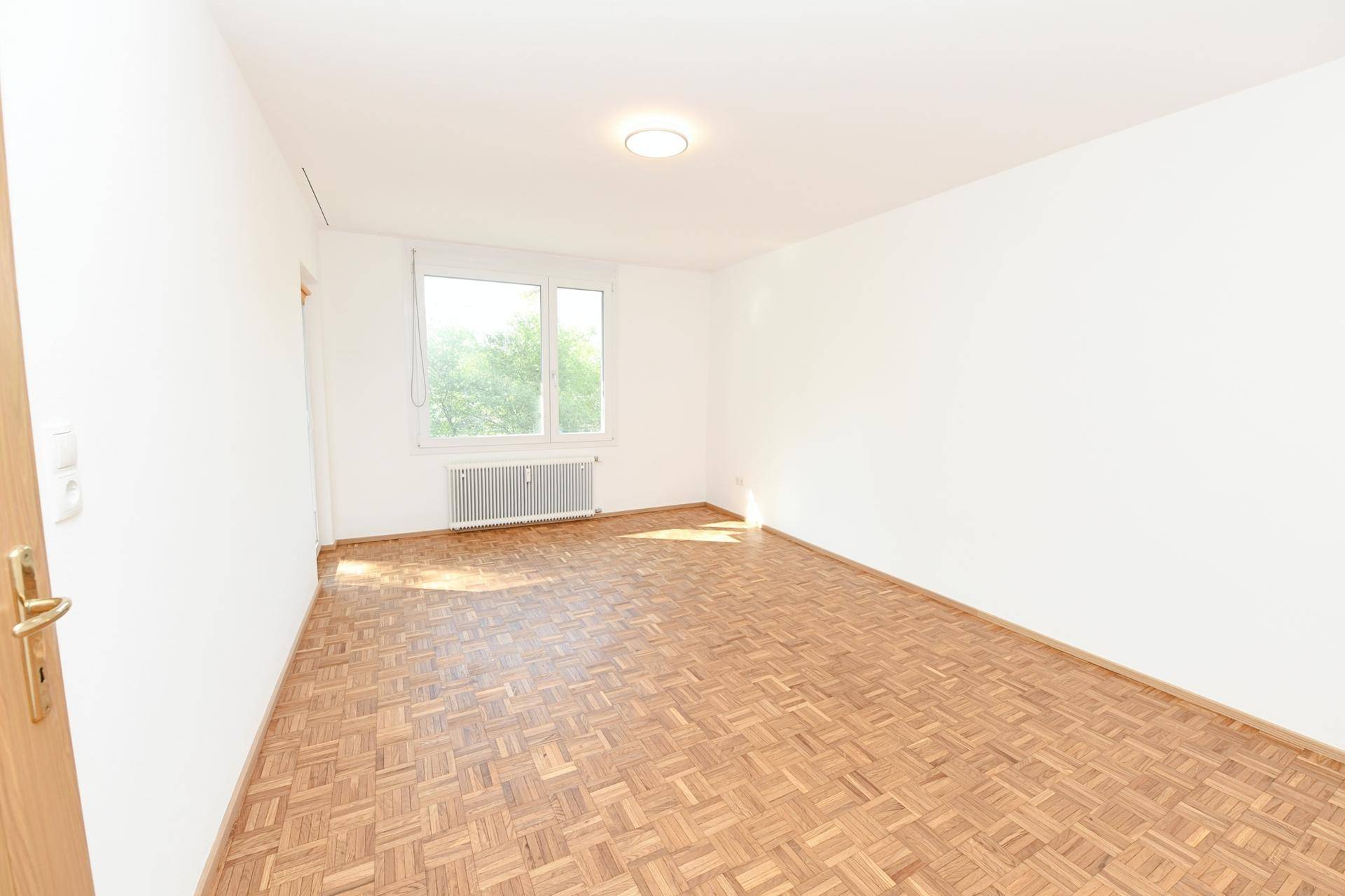 Sonniger Raum mit Parkettboden und großem Fenster, ideal als Schlaf- oder Arbeitszimmer.