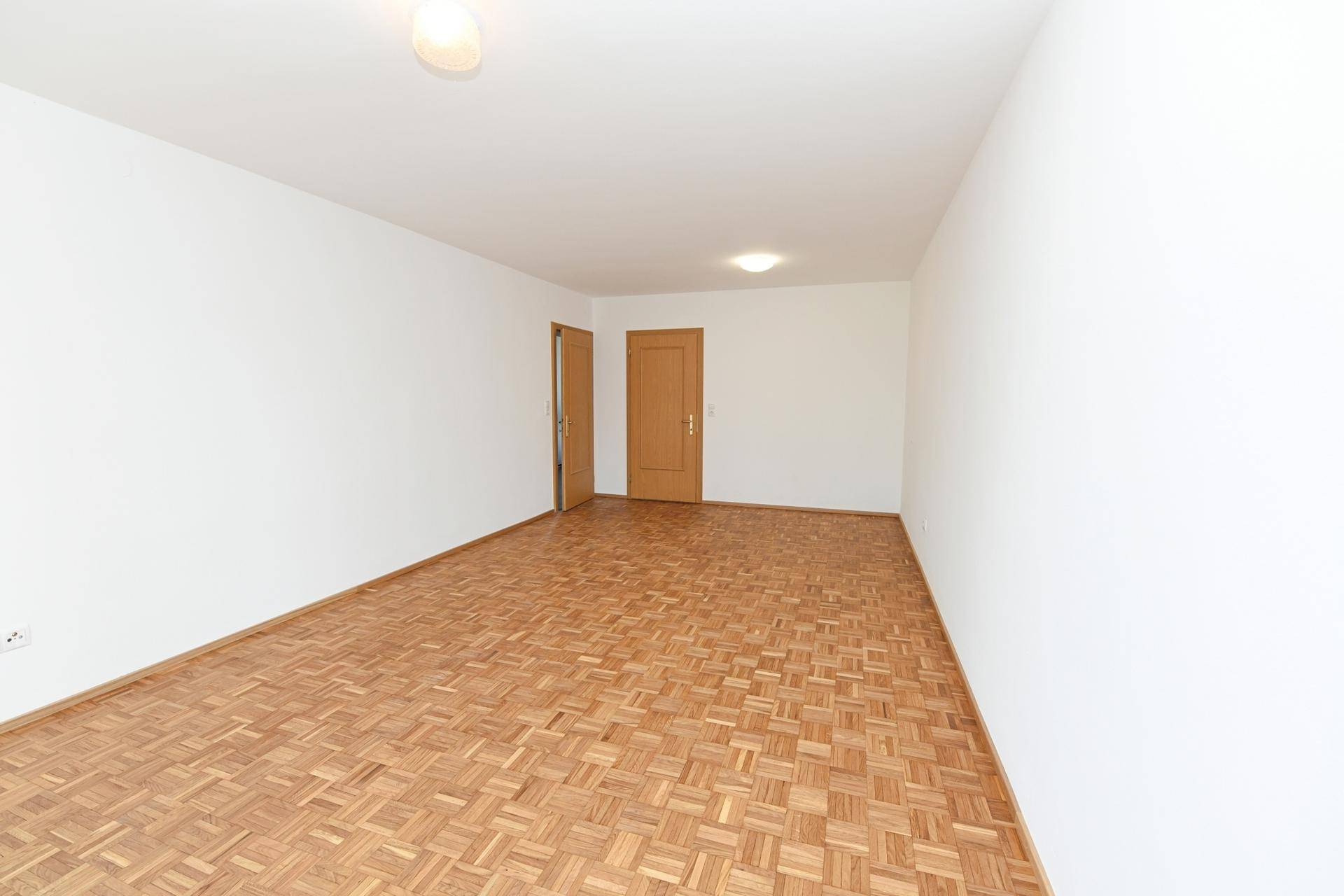 Leeres Zimmer mit Parkettboden und zwei Holztüren, bietet vielseitige Nutzungsmöglichkeiten.