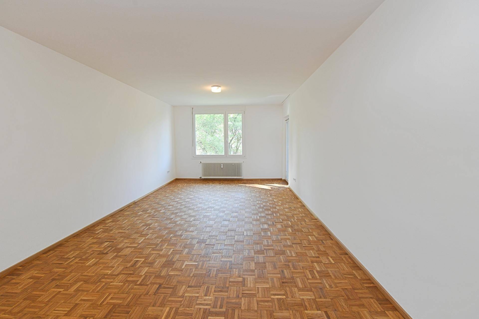 Helles, leeres Zimmer mit Fischgrätparkett und großem Fenster, bereit zur individuellen Gestaltung.
