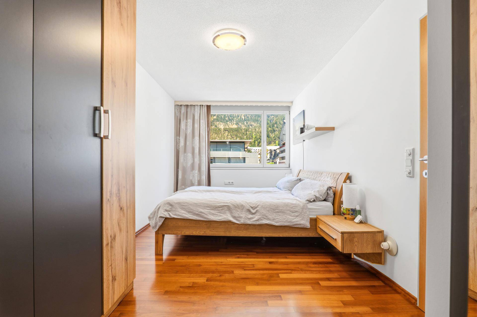 Gemütliches Schlafzimmer mit Holzbett, Kleiderschrank und Fenster mit Bergblick.