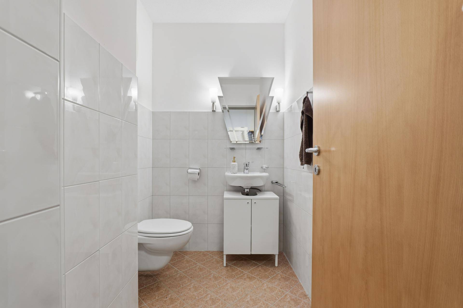 Separates Gäste-WC mit kleinem Waschbecken und Toilette, hell gefliest.