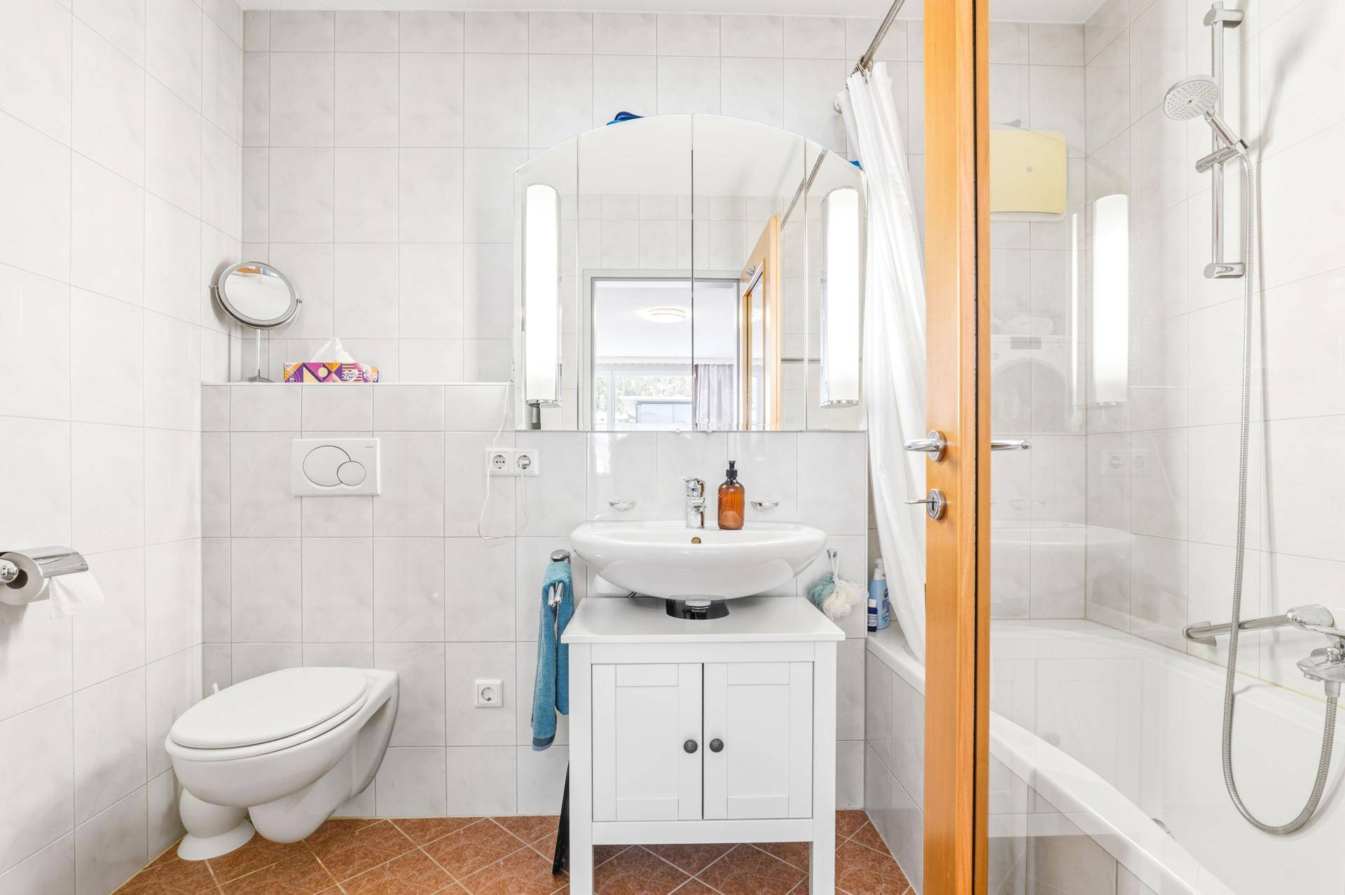 Helles Badezimmer mit Badewanne, Dusche, WC und Waschbecken mit Spiegelschrank.