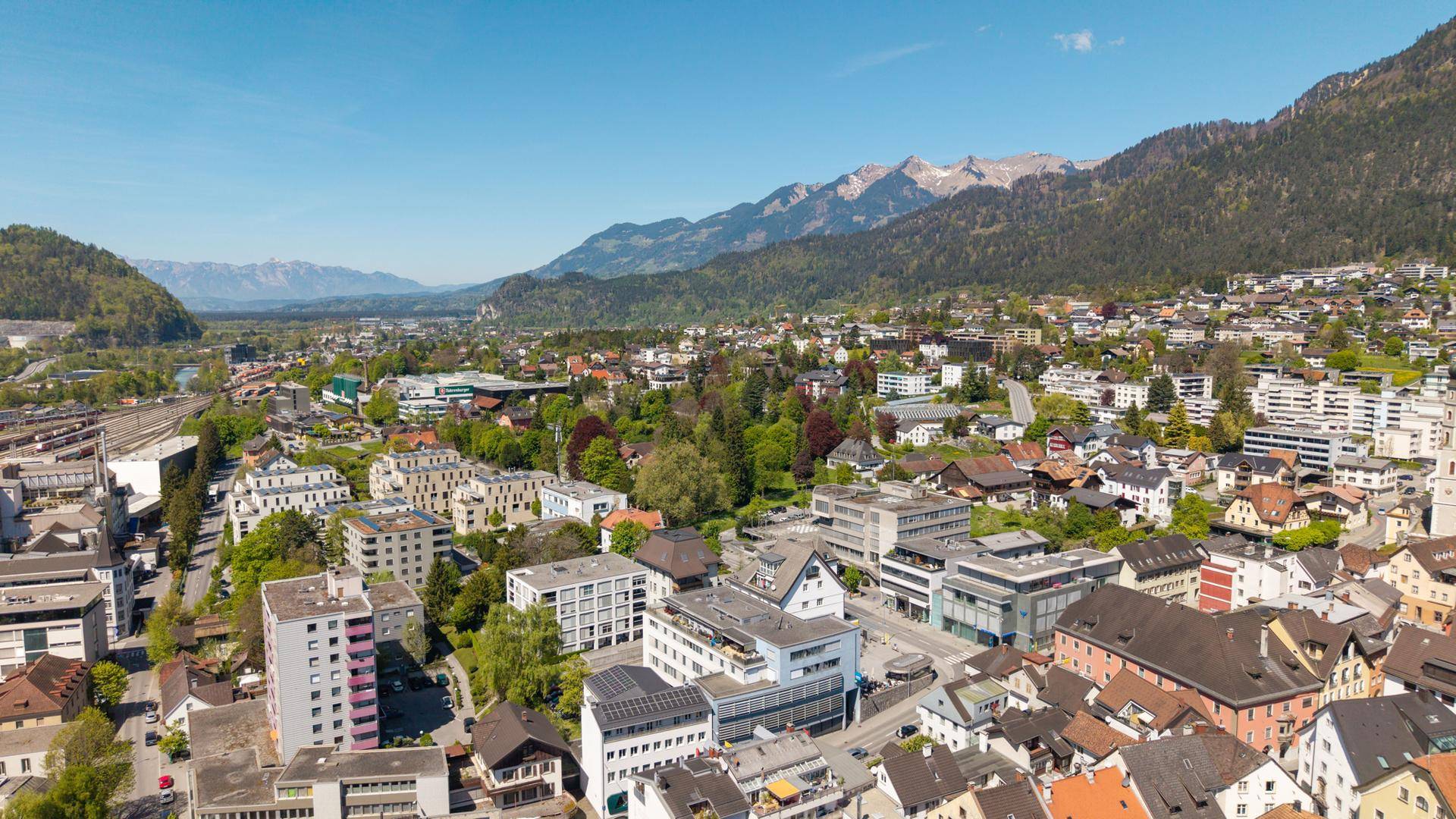 Ausgedehnte Luftaufnahme einer Stadt in einer Berglandschaft unter blauem Himmel.