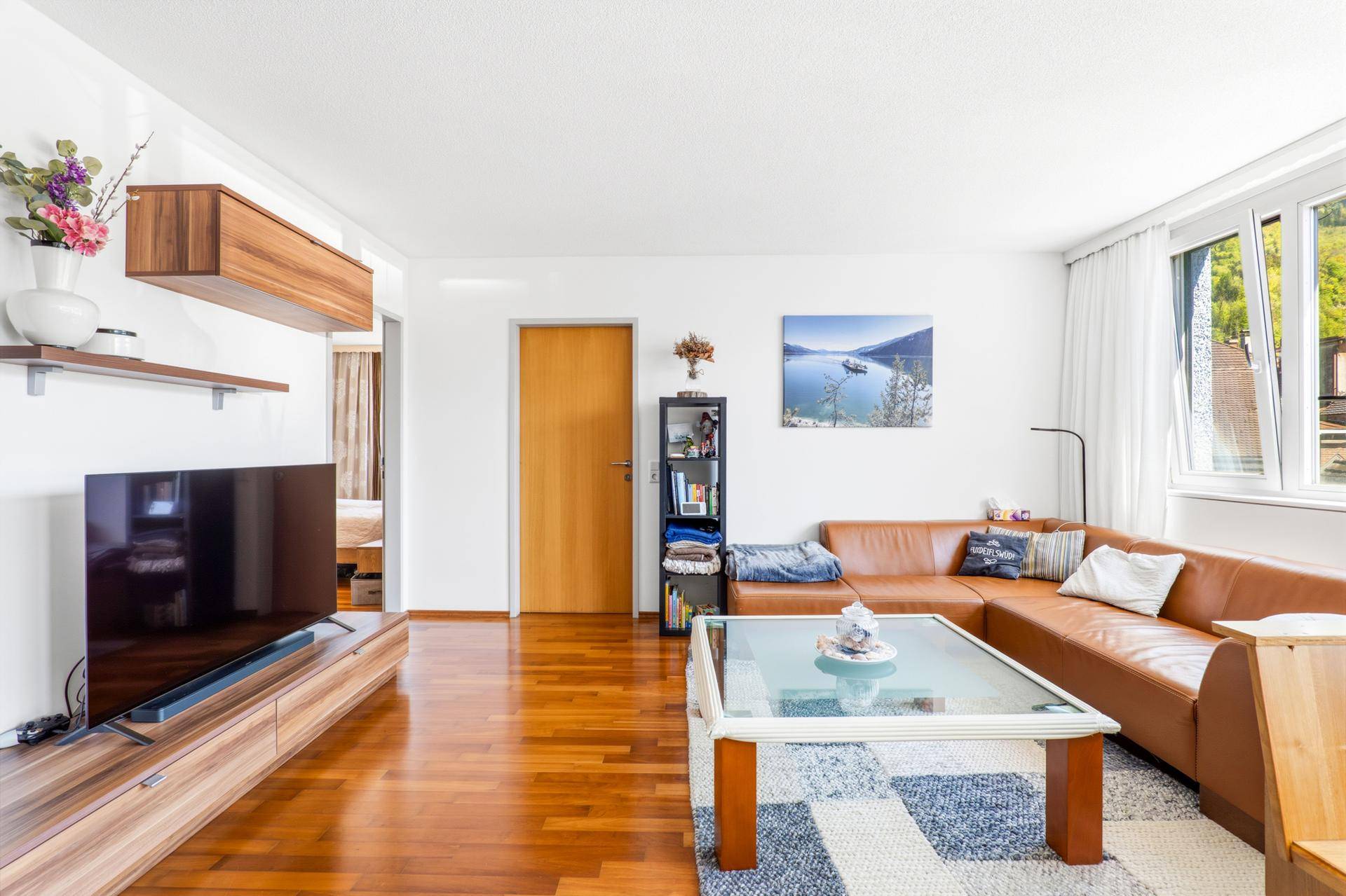 Gemütliches Wohnzimmer mit Ledersofa, Holzboden und Blick auf die umliegende Landschaft.