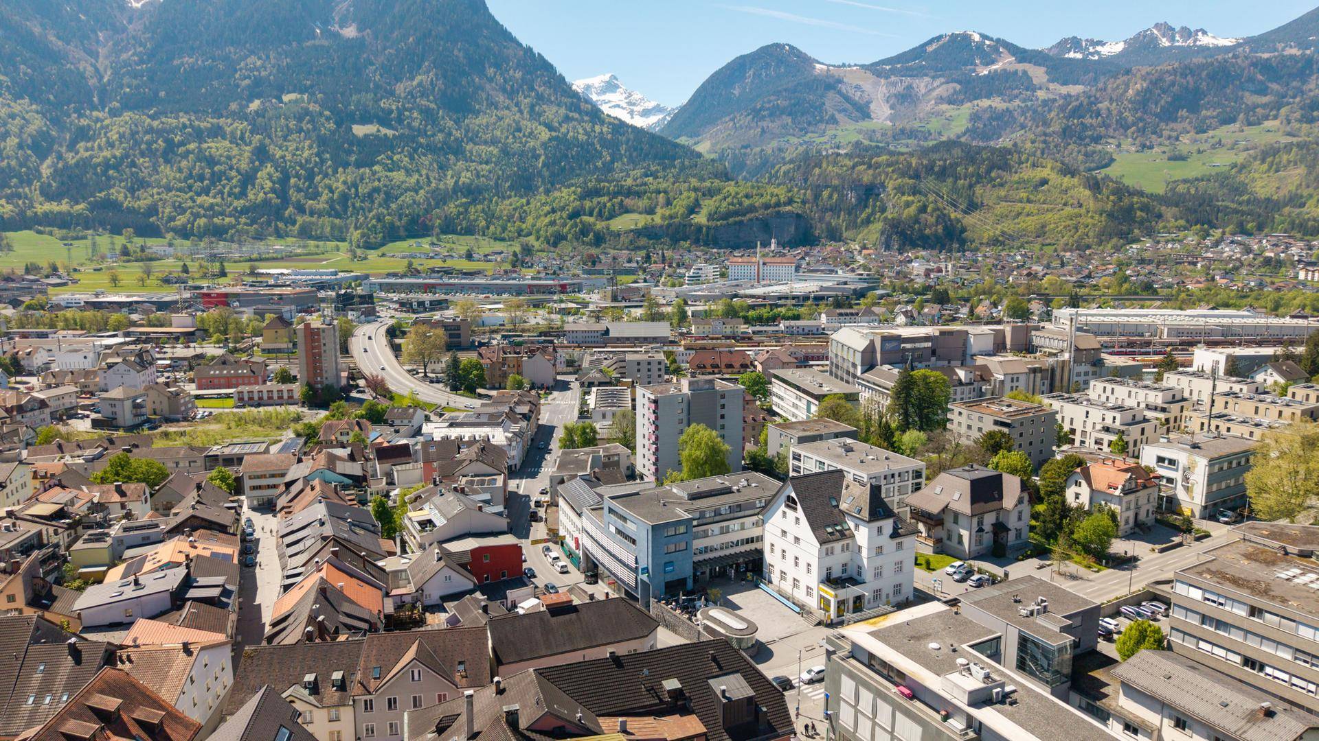 Weitläufige Luftaufnahme einer Stadtlandschaft mit majestätischen Bergen im Hintergrund.