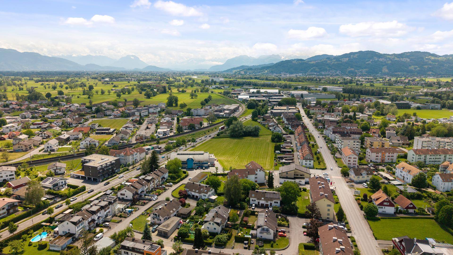 Panoramablick aus der Vogelperspektive auf eine Wohngegend, umgeben von Natur und Berglandschaft.