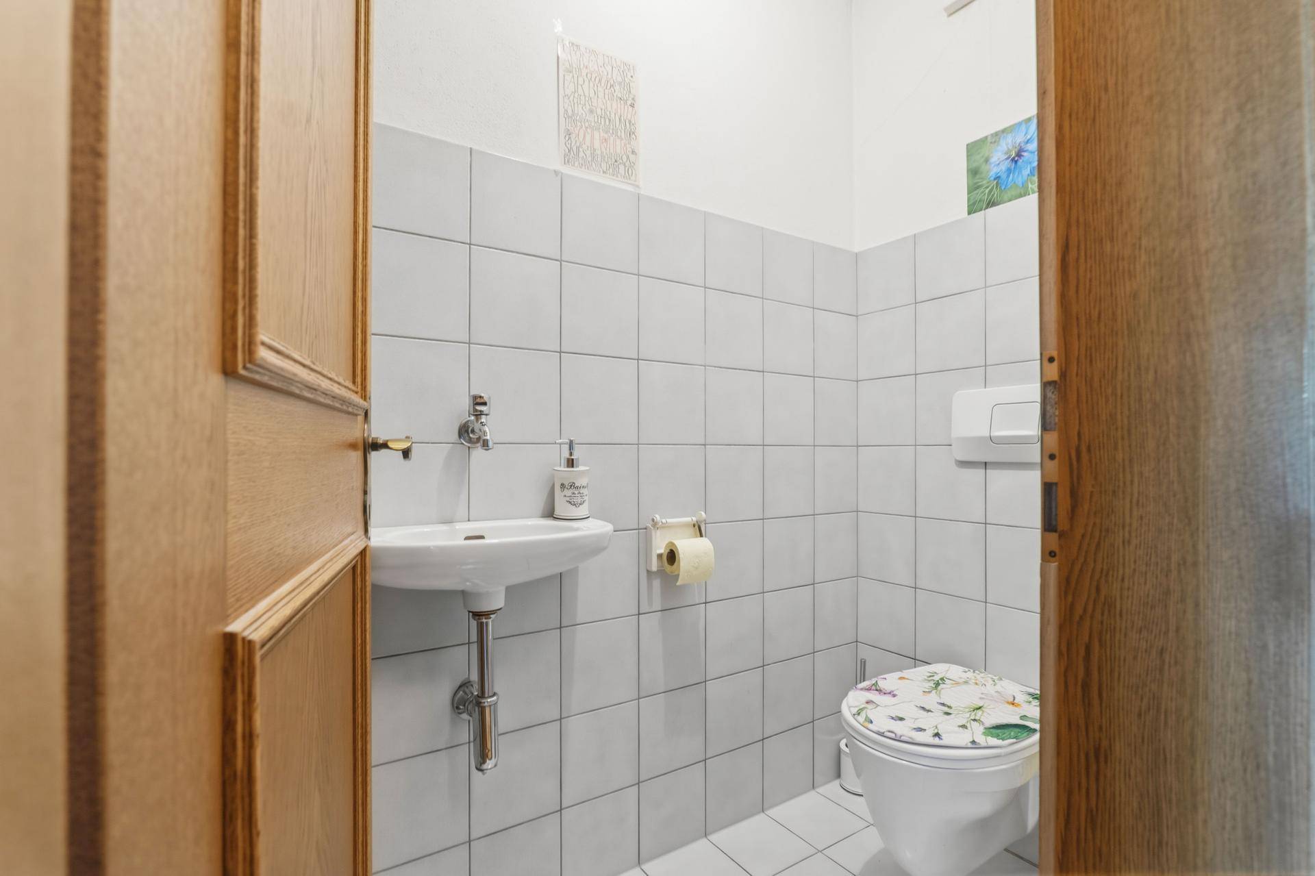 Helles Gäste-WC mit weißen Fliesen, kleinem Waschbecken und Toilette.