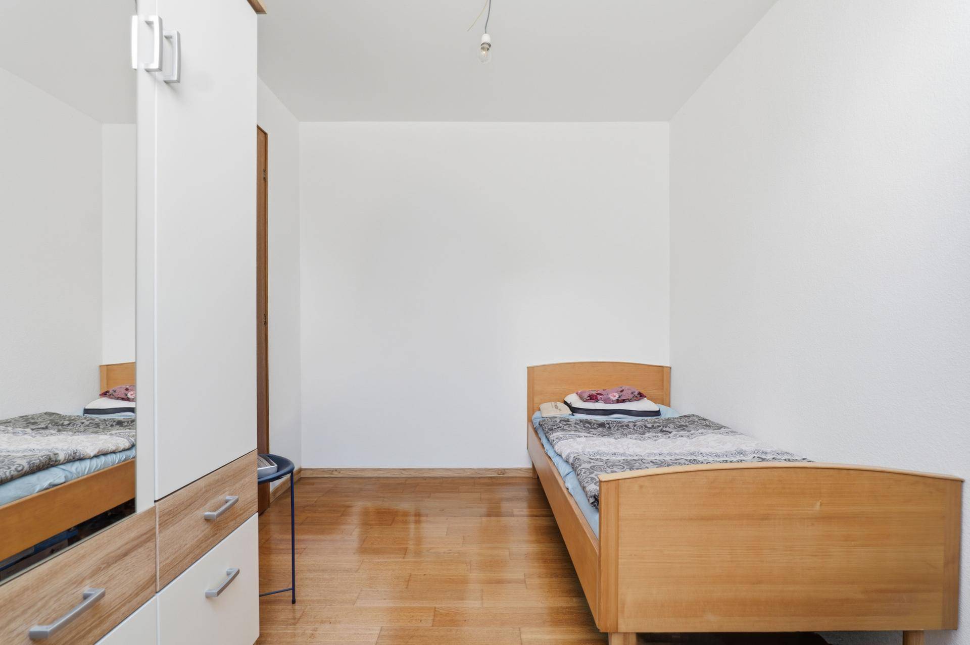 Einfaches Schlafzimmer mit Einzelbett und weißem Kleiderschrank.