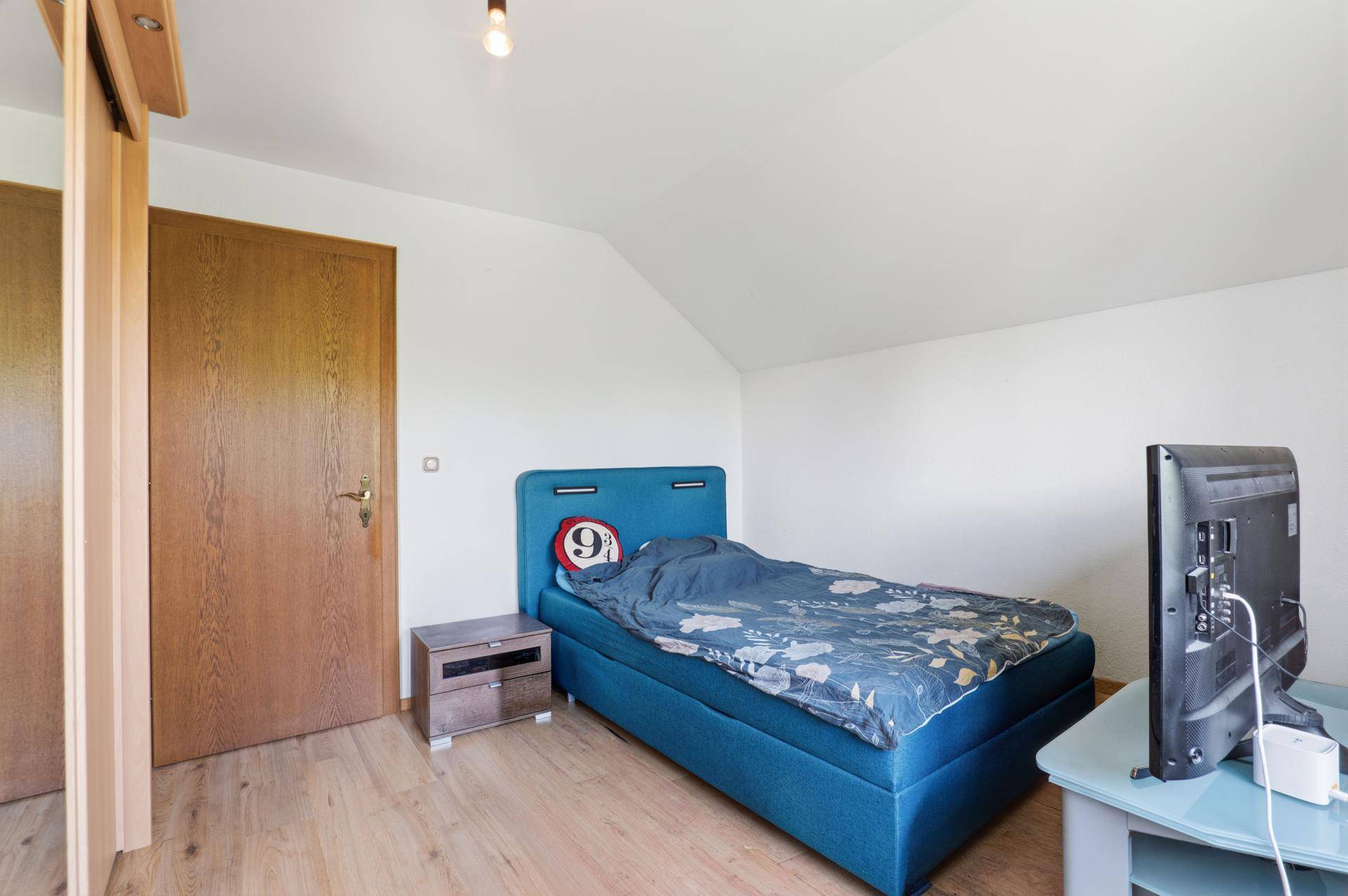 Gemütliches Schlafzimmer mit Einzelbett, Nachttisch und Holztür.