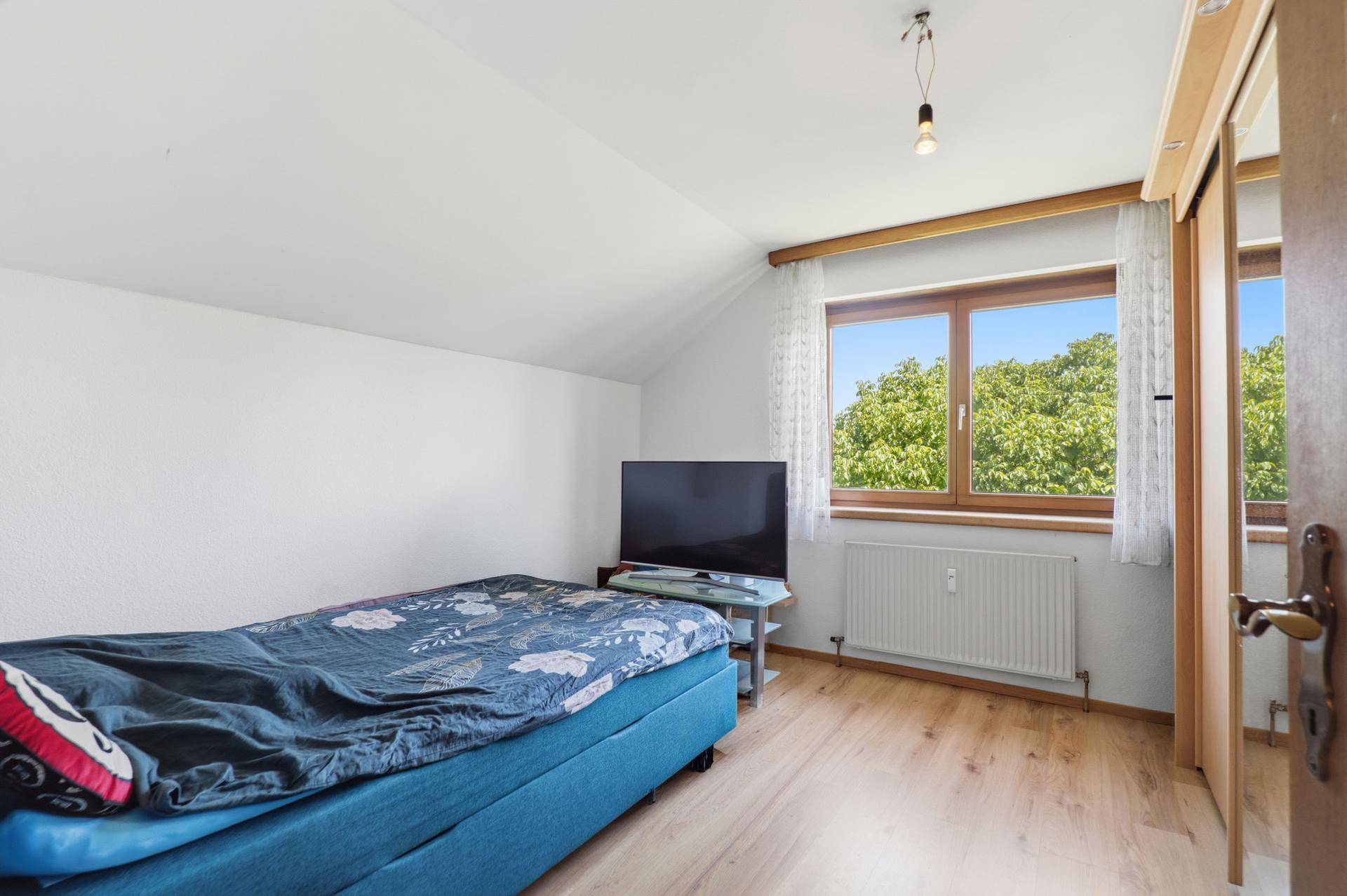 Schlafzimmer mit Einzelbett, Fernseher und Fenster mit Blick ins Grüne.