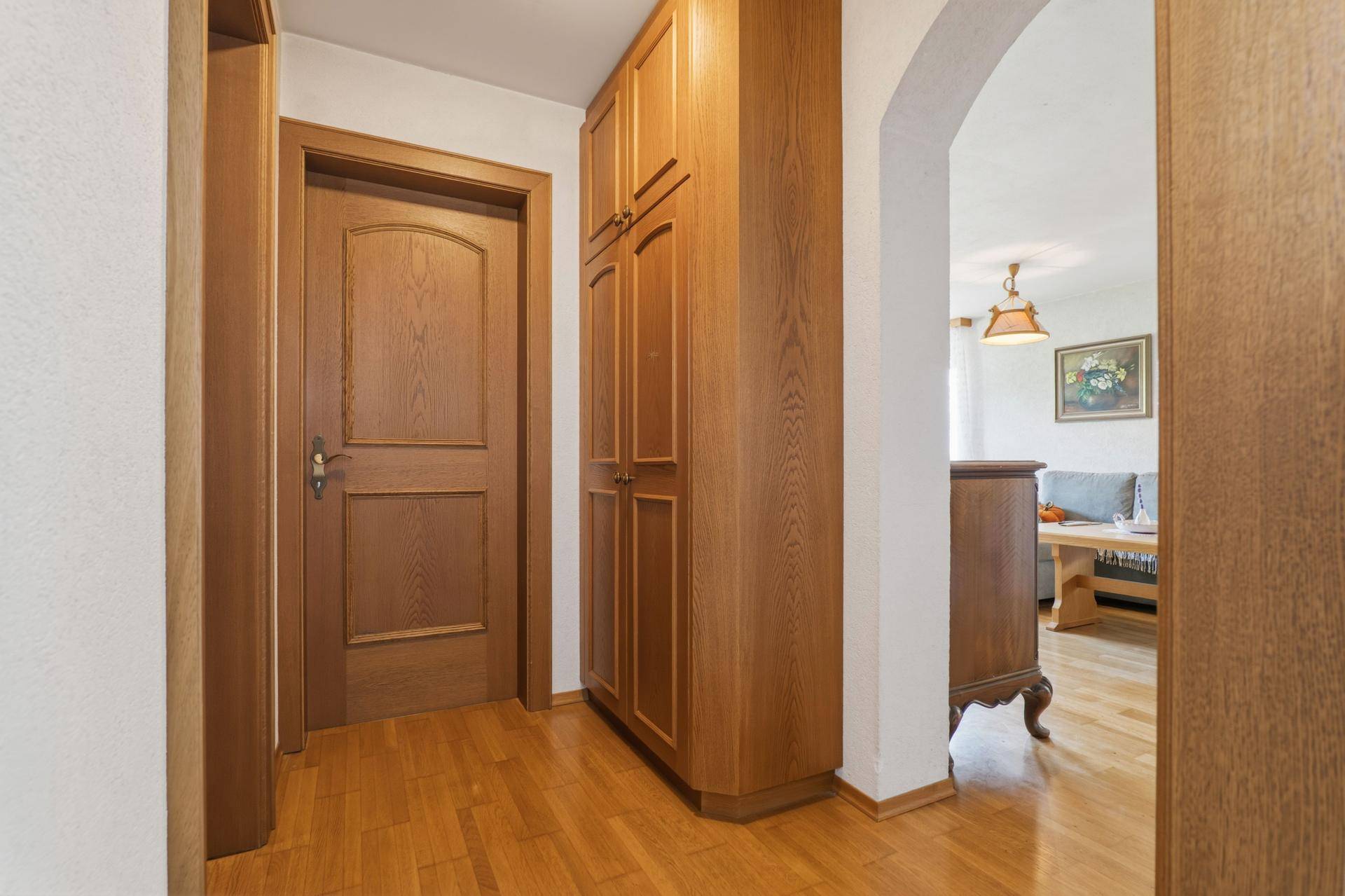Flur mit Holzfußboden, Einbauschrank und offenem Durchgang zum Wohnbereich.
