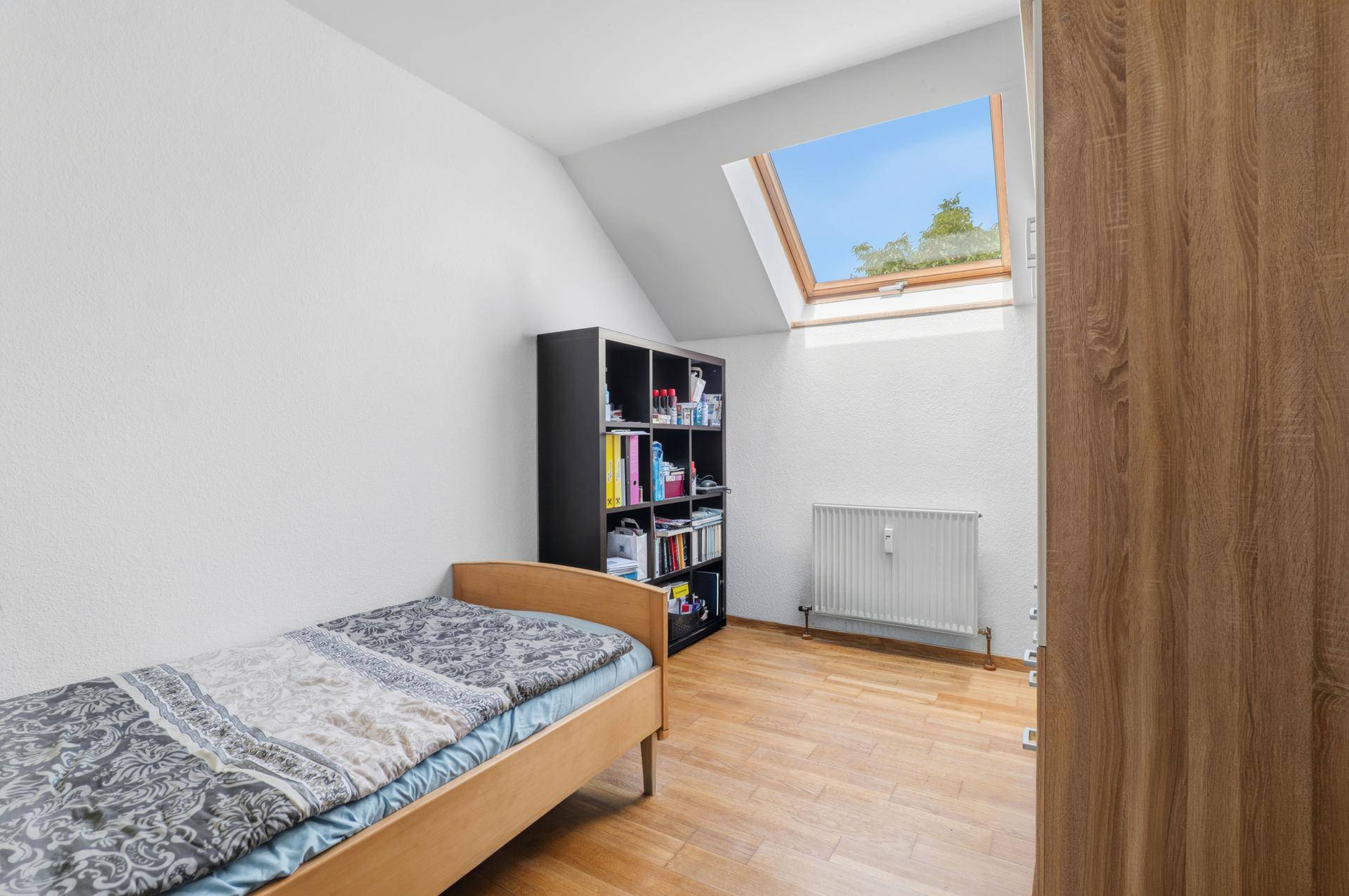 Schlafzimmer mit Einzelbett, Bücherregal und Dachfenster für viel Tageslicht.