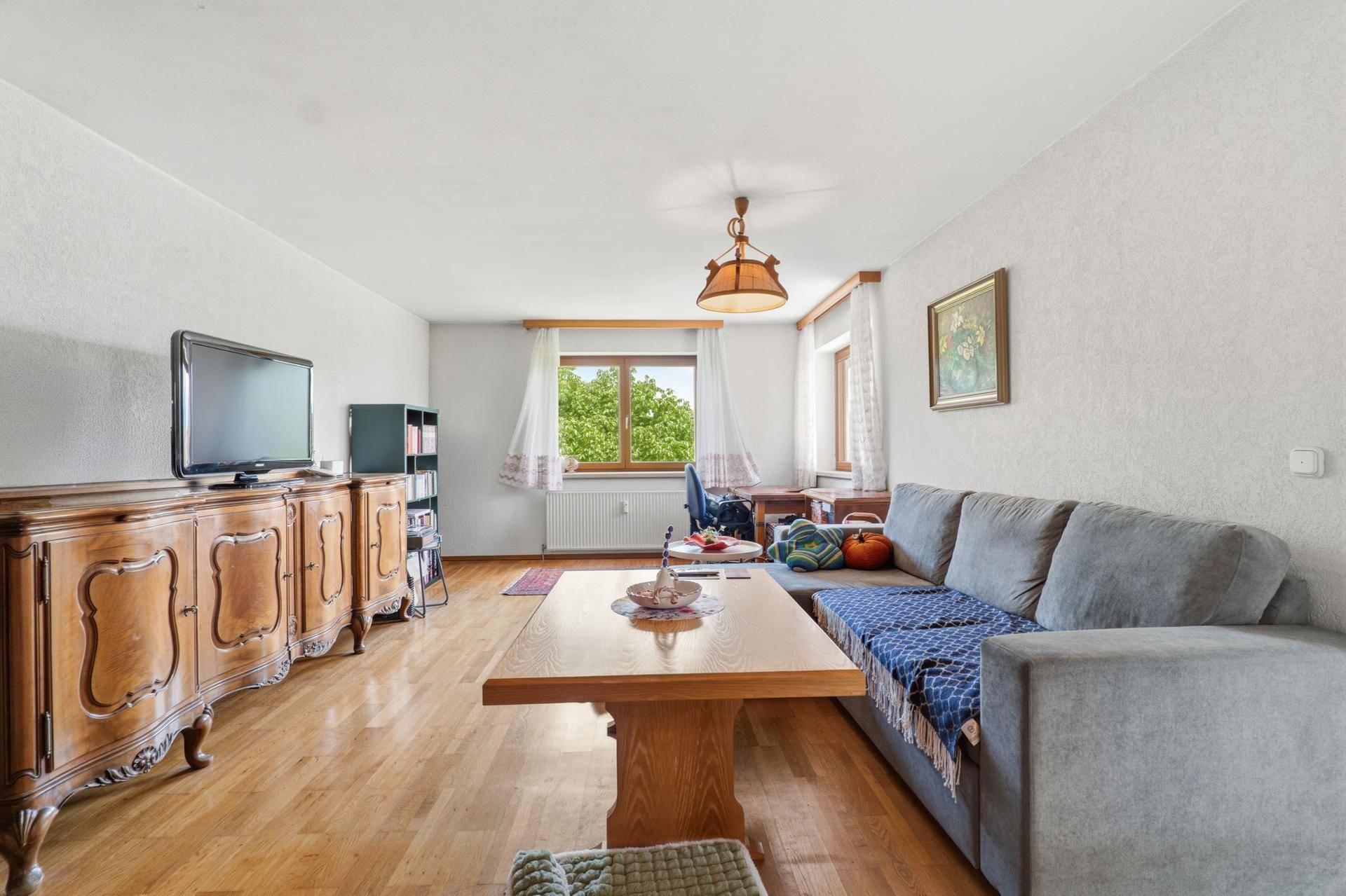 Helles Wohnzimmer mit bequemer Couch, Holztisch und Blick ins Grüne durch das Fenster.