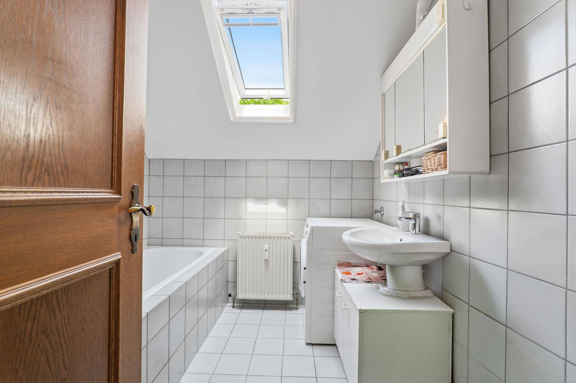 Helles Badezimmer mit Badewanne, Waschbecken, Waschmaschine und Dachfenster.