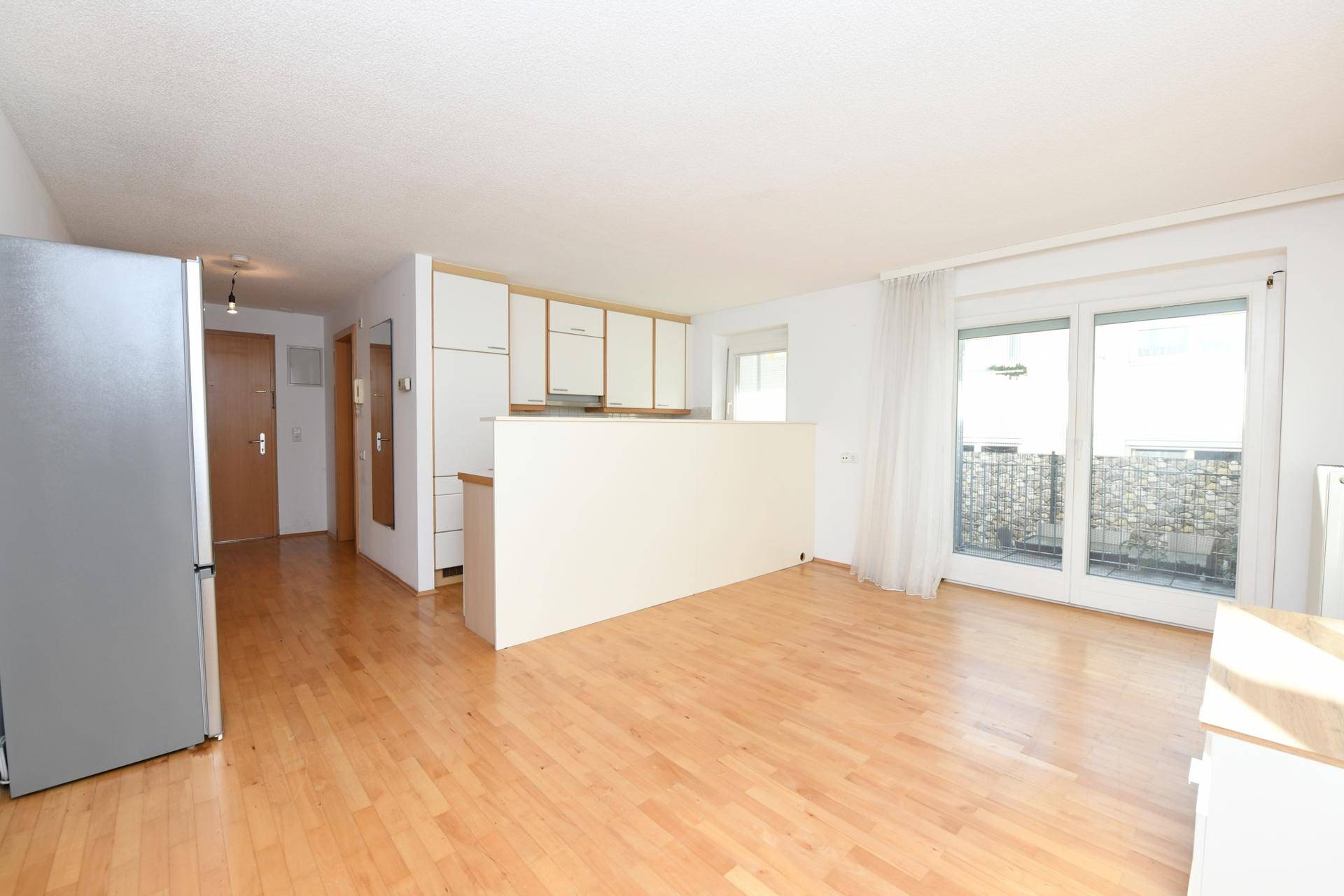 Geräumiger, heller Wohnbereich mit Holzboden und großem Fenster zum Balkon.