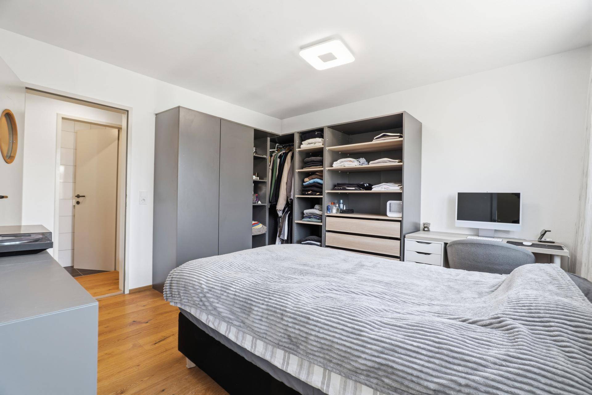 Schlafzimmer mit großem Bett, Holzboden und offenem Kleiderschranksystem.