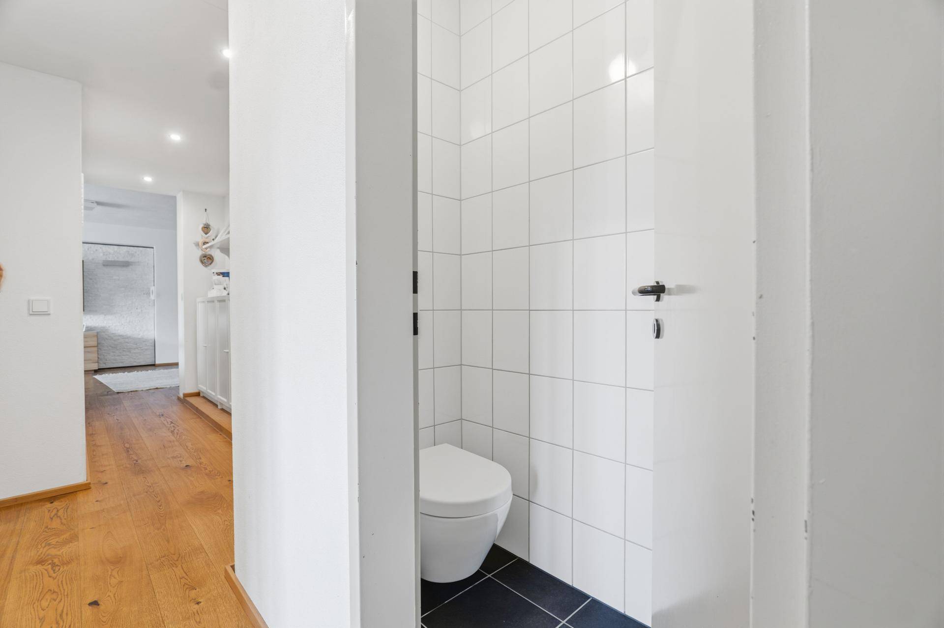 Separates WC mit Wandtoilette und weißen Fliesen.