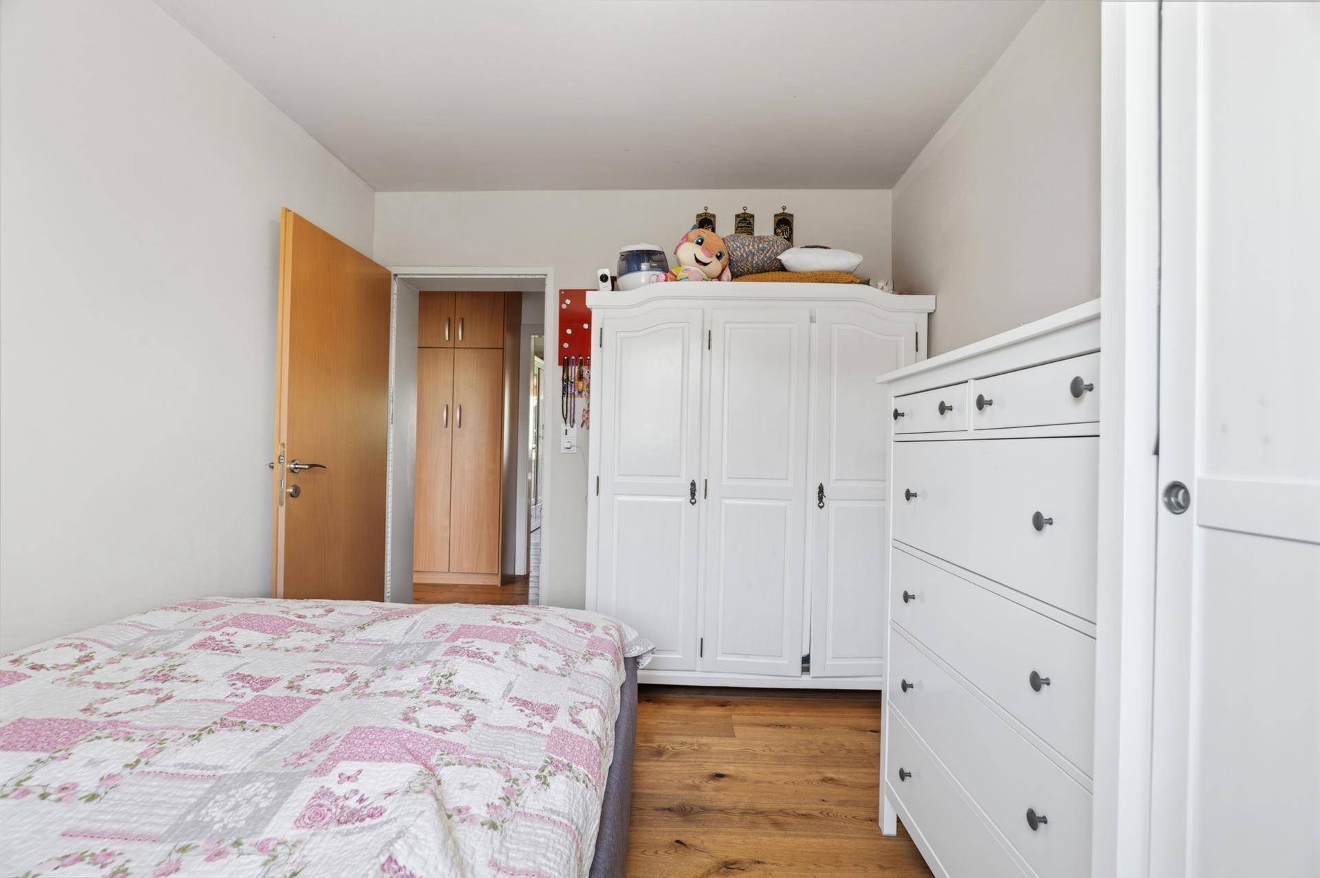Kinderzimmer mit Bett, weißem Kleiderschrank und Holzboden.