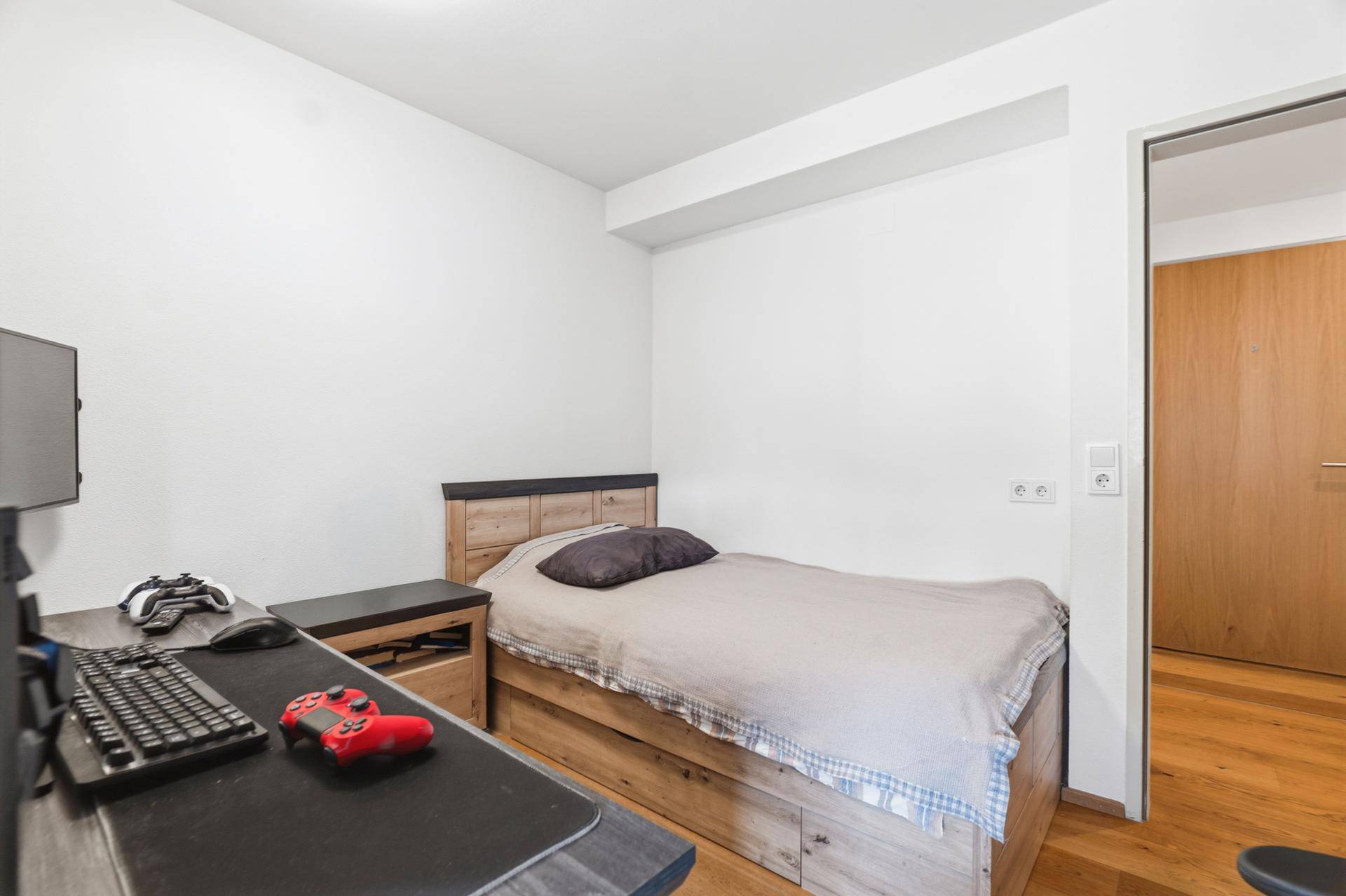 Kleines Schlafzimmer mit Holzbett, Schreibtisch und Holzboden.