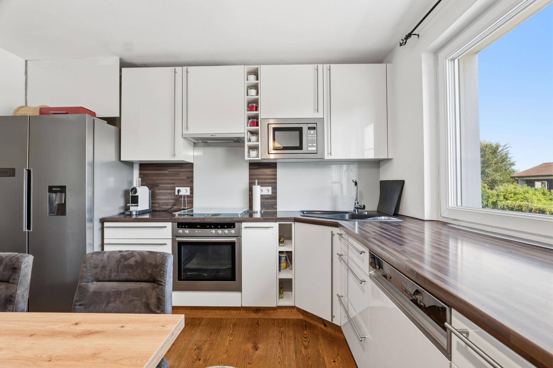 Moderne Küche mit weißen Hochglanzfronten, Holzarbeitsplatte und Fenster.