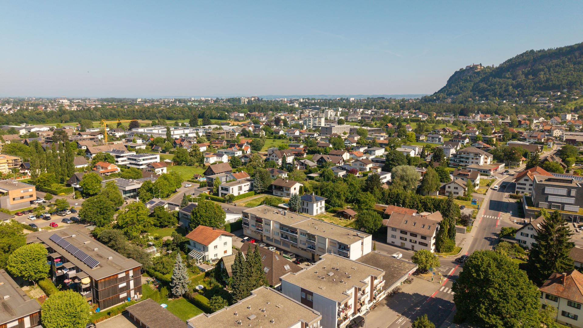 Luftaufnahme einer Wohnsiedlung mit weitem Blick über die Stadt bis zum Horizont und einem See in der Ferne.