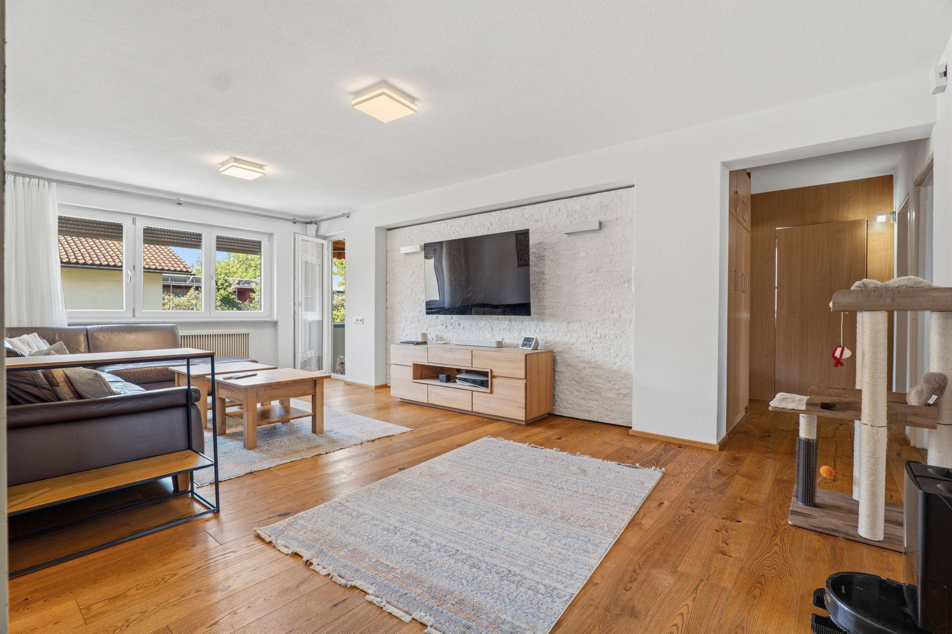 Geräumiges Wohnzimmer mit Holzboden, großem Fernseher und Zugang zum Balkon.