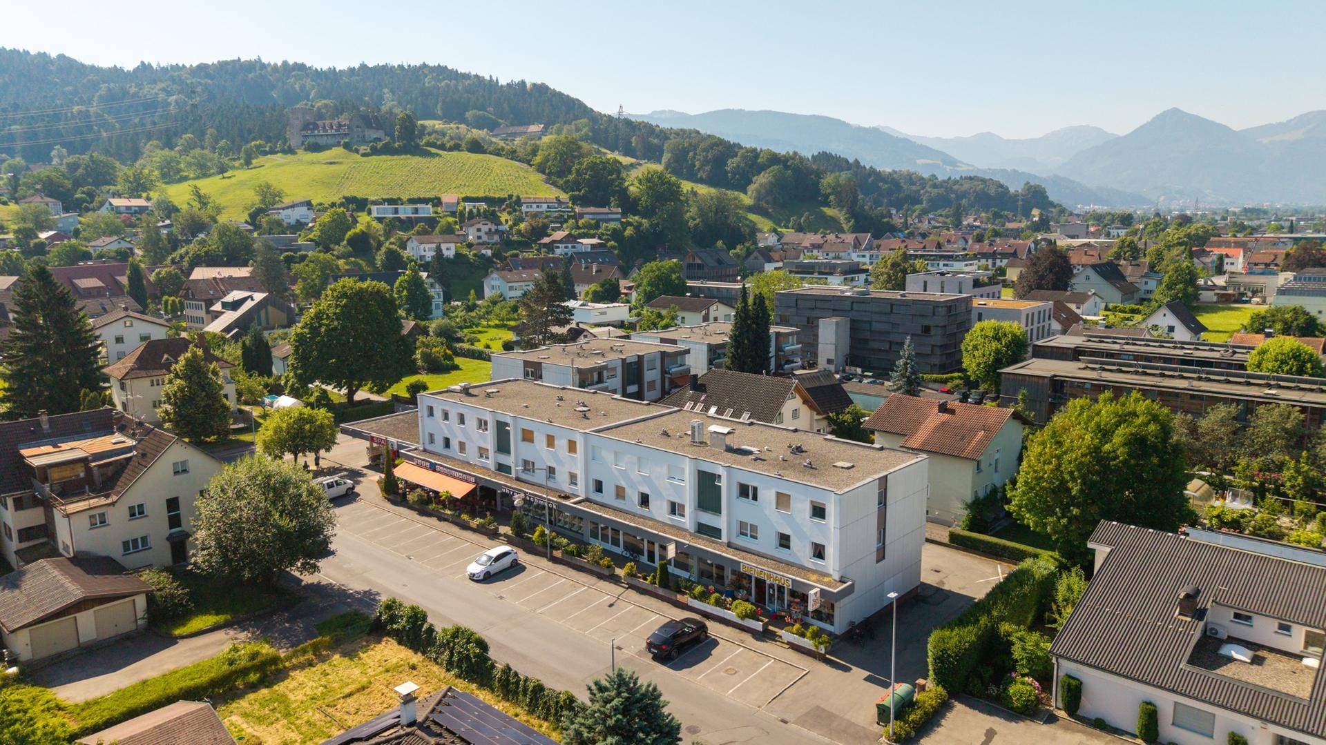 Weitläufige Luftaufnahme eines Gebäudekomplexes in einer Stadt mit grünen Hügeln im Hintergrund.
