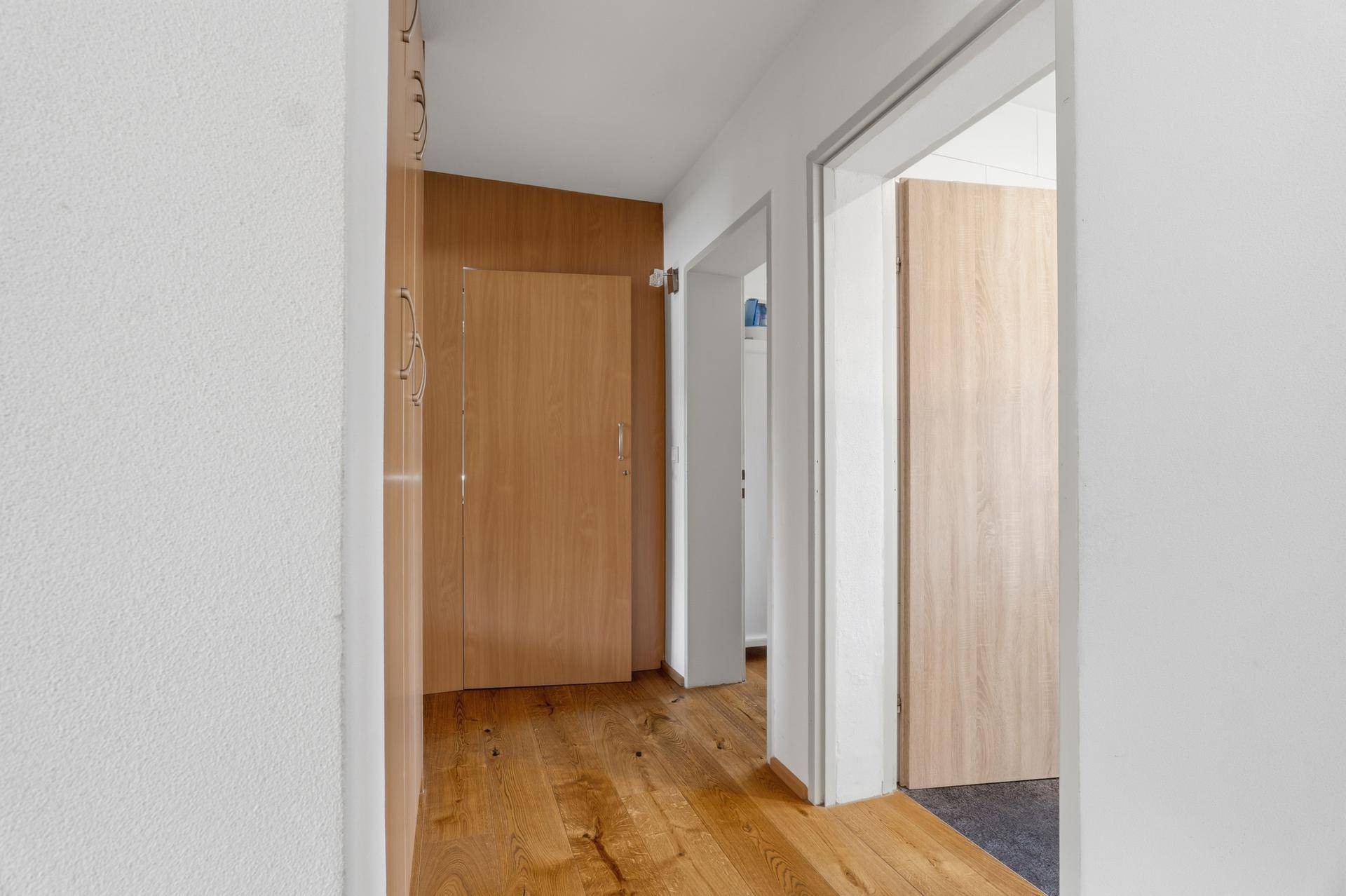 Heller Flur mit Holzboden und Zugang zu verschiedenen Zimmern.