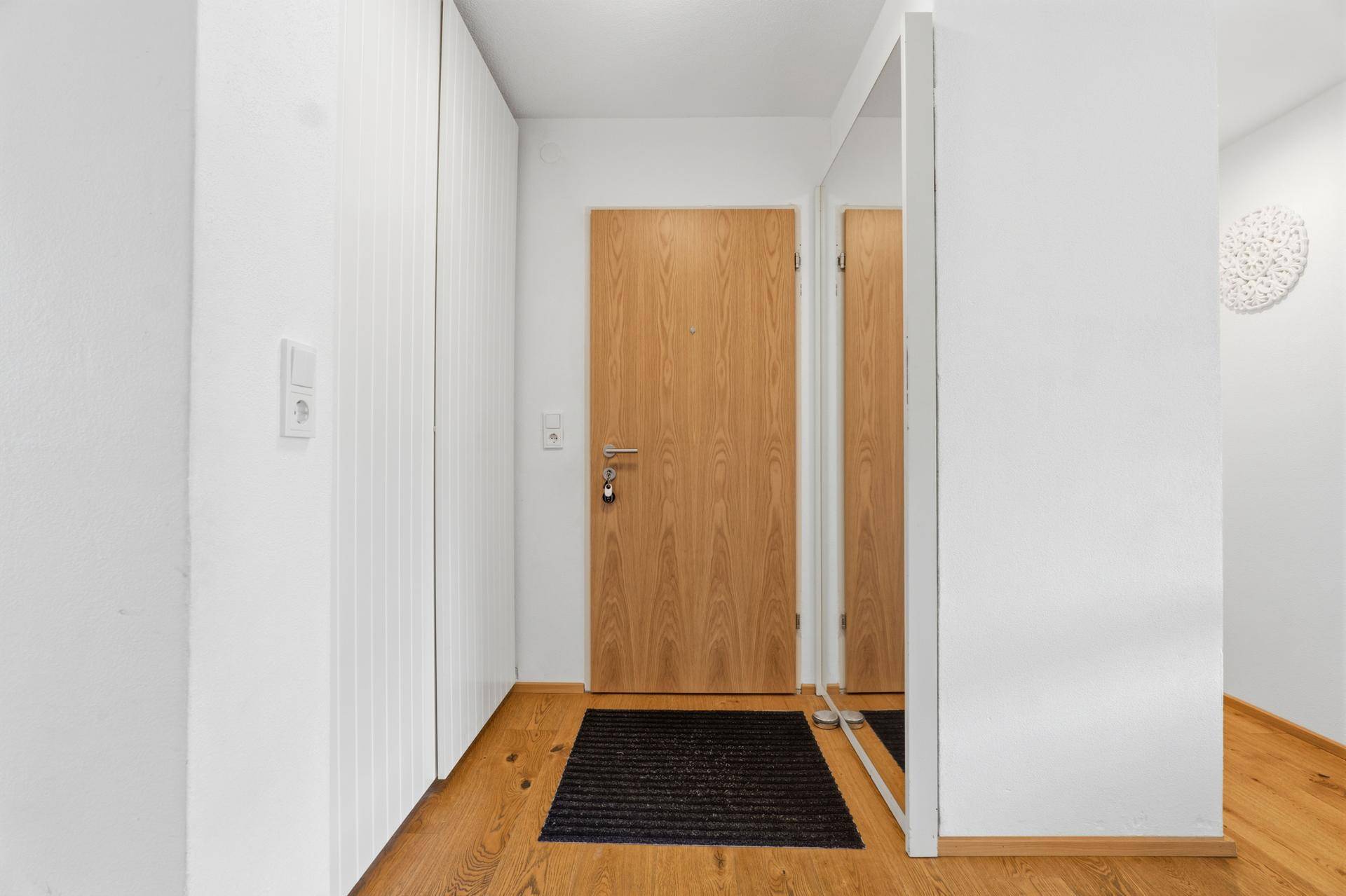 Eingangsbereich mit Holztür, großem Spiegel und Holzboden.