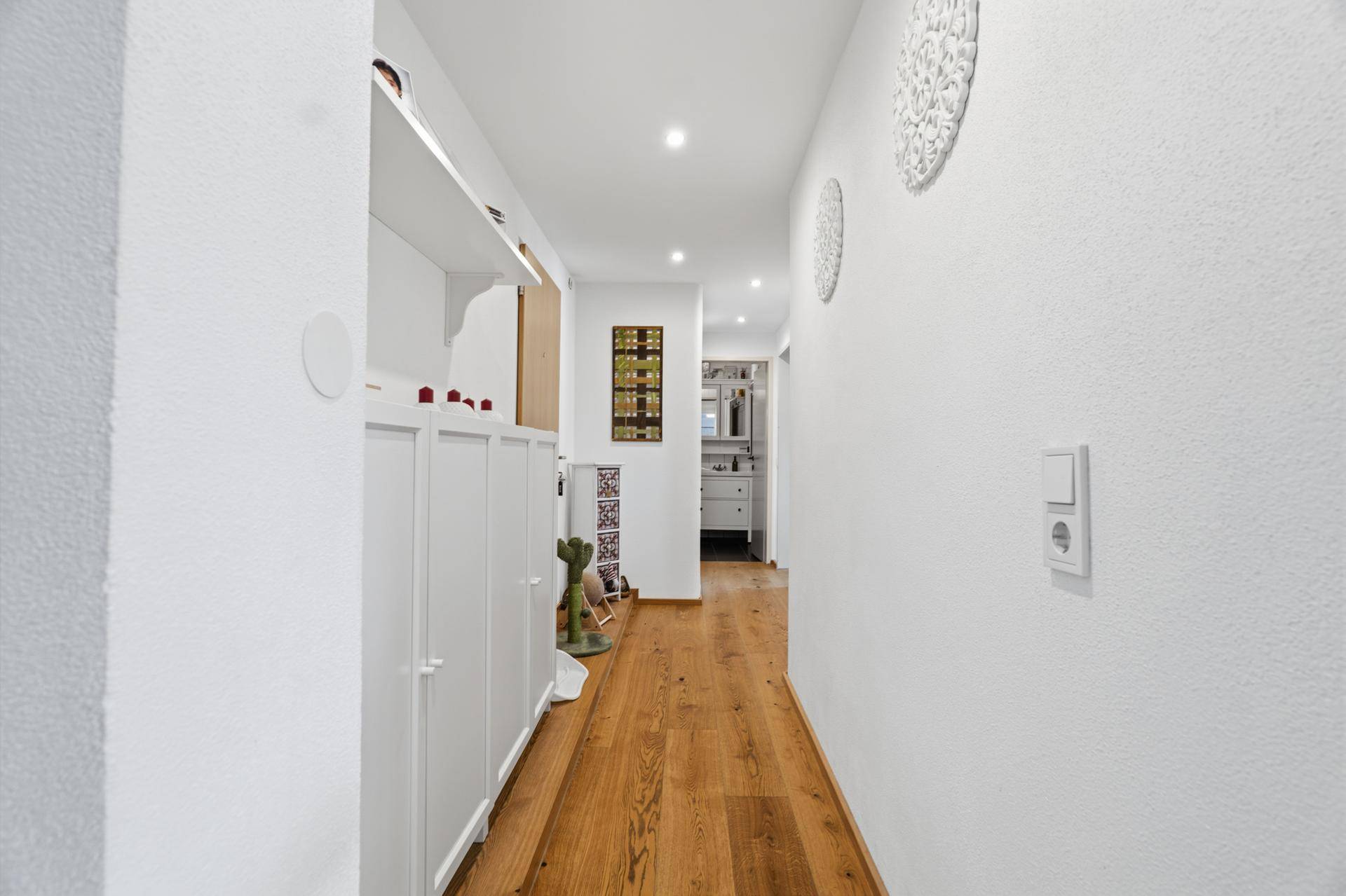 Langer Flur mit Einbauschränken, Holzboden und Blick ins Badezimmer.