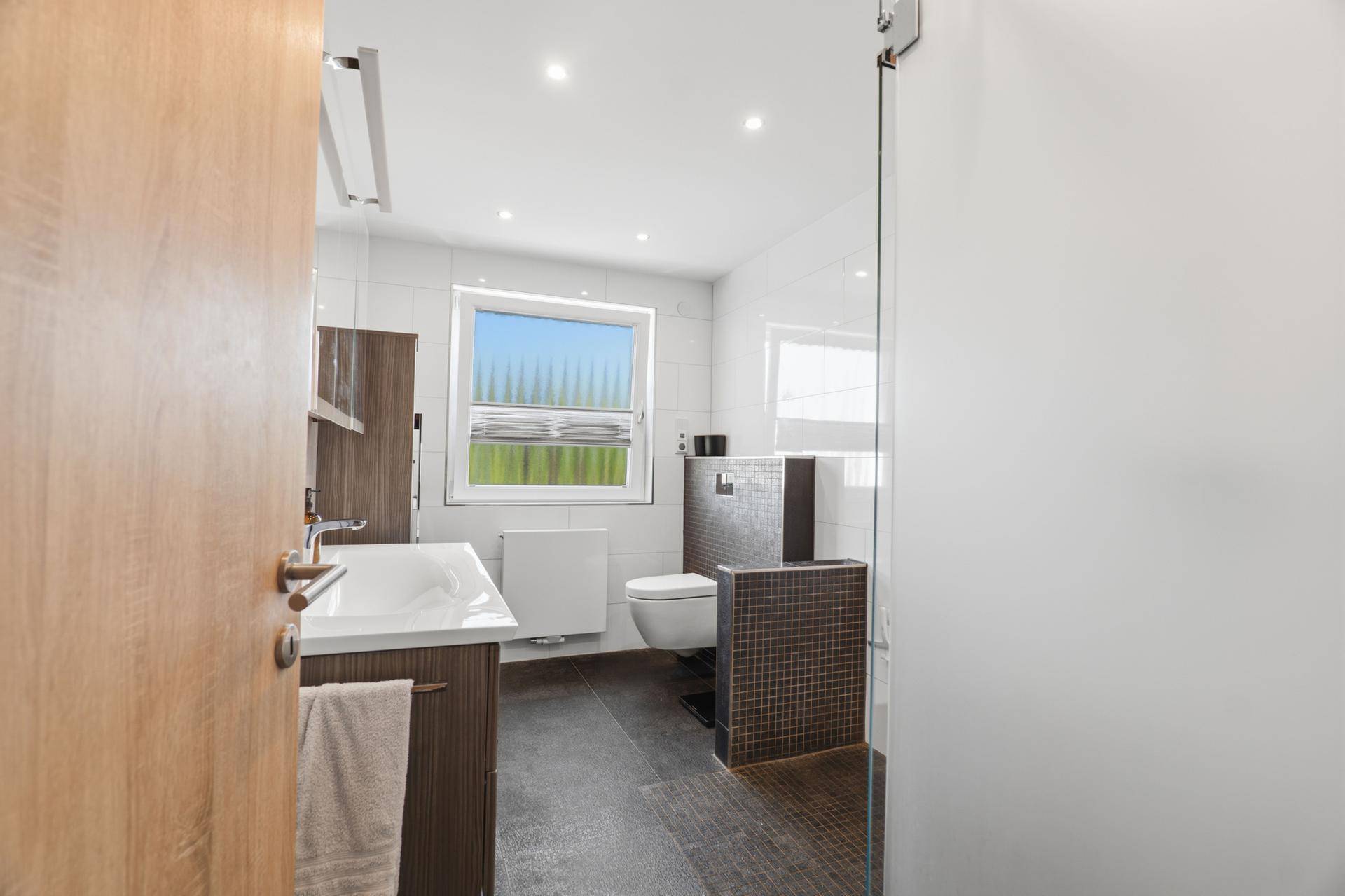 Modernes Badezimmer mit Dusche, WC, Einzelwaschbecken und Fenster.