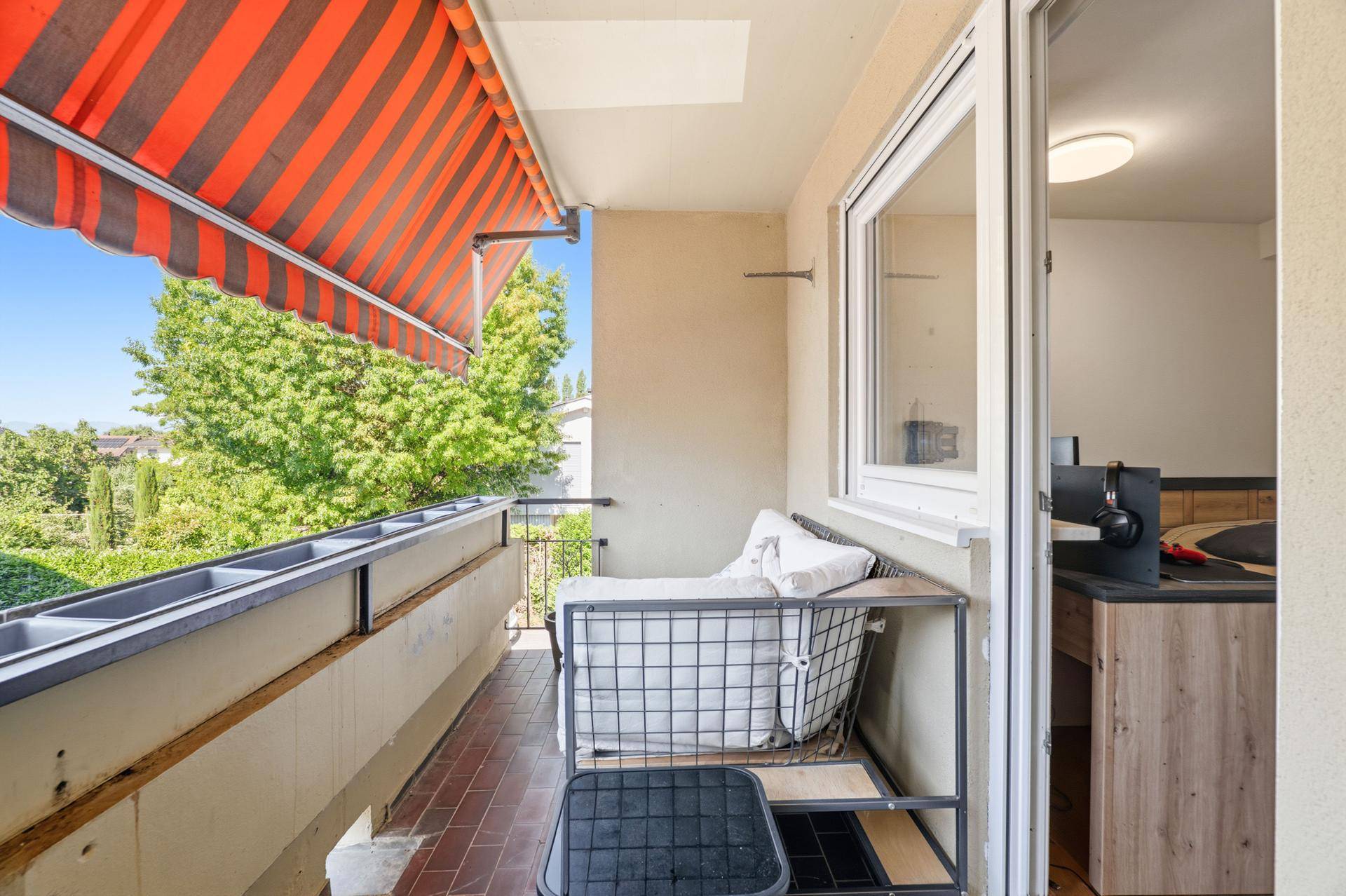 Balkon mit Markise, Sitzgelegenheit und Blick auf Bäume.