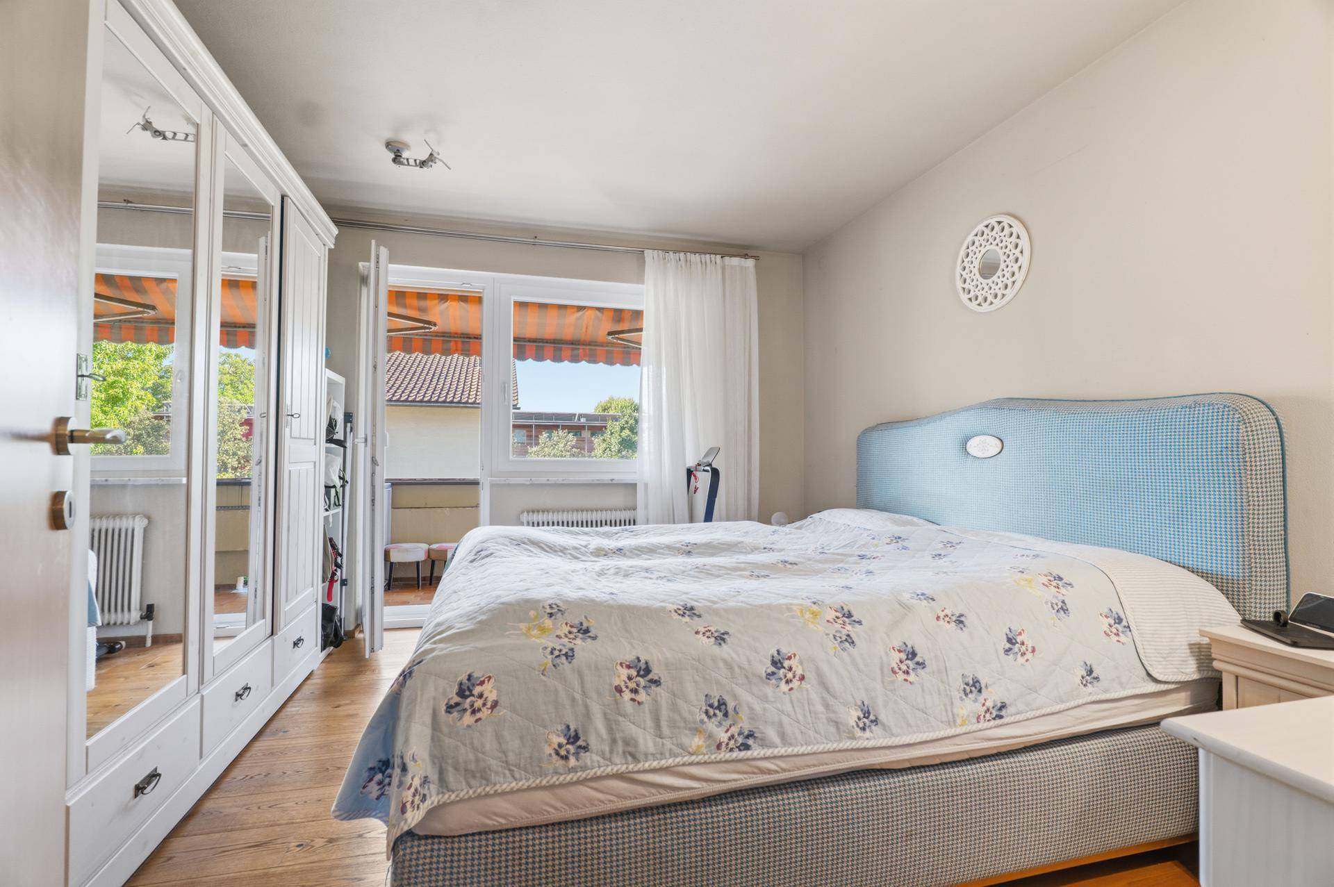 Helles Schlafzimmer mit Doppelbett, Spiegelschrank und Balkonzugang.