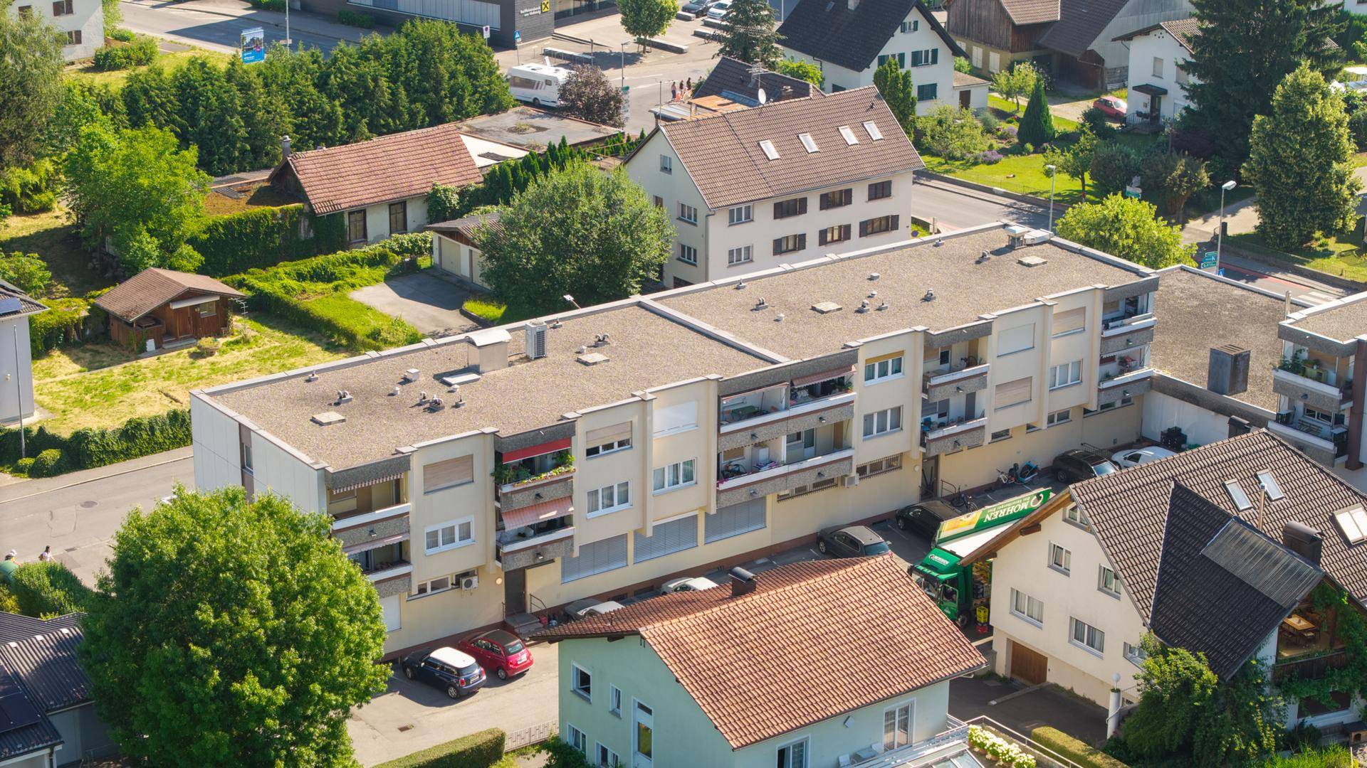 Luftaufnahme eines Mehrfamilienhauses mit Flachdach und Balkonen in einer Wohngegend.