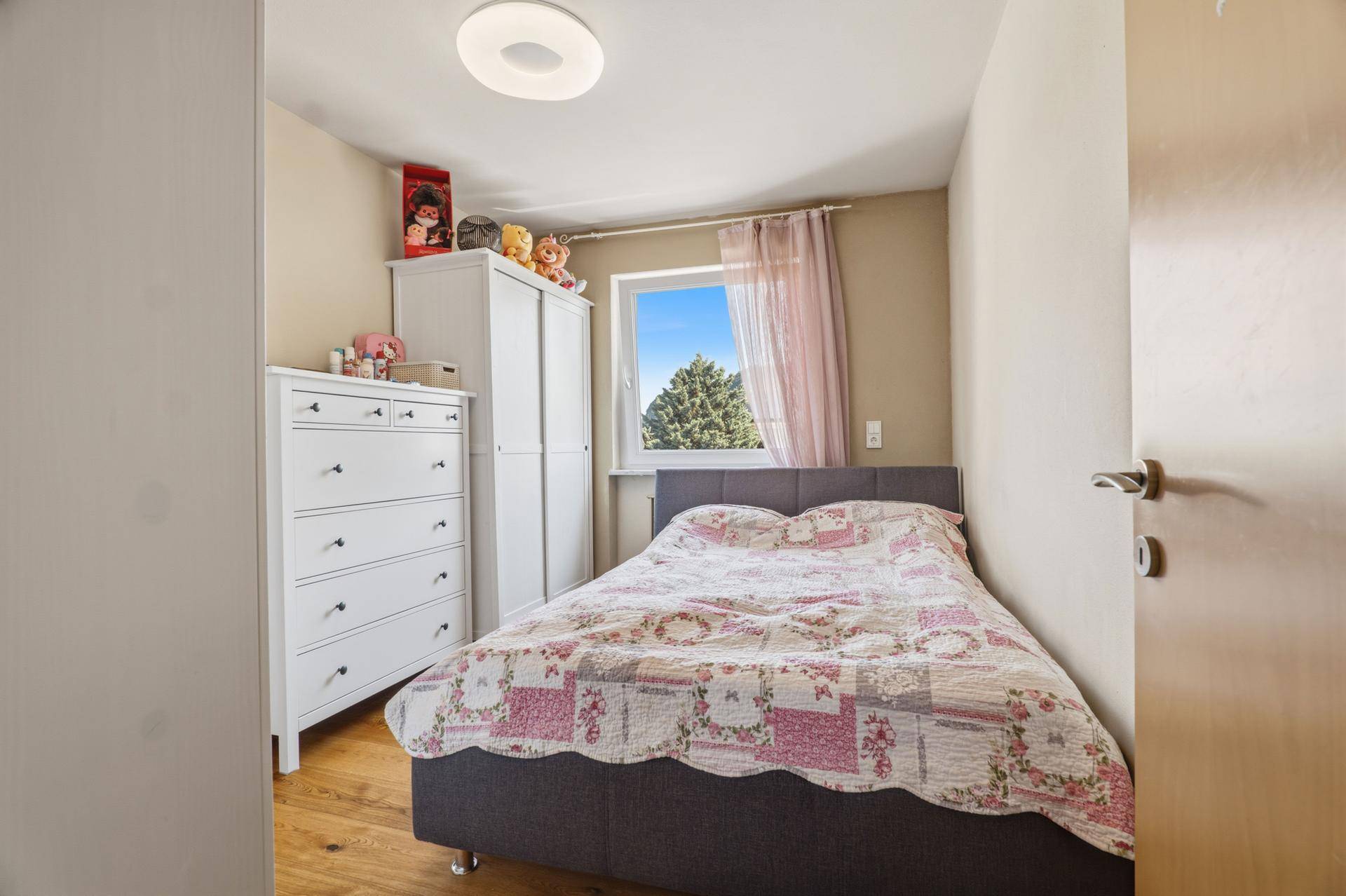 Kinderzimmer mit Einzelbett, weißer Kommode und Fenster mit Blick ins Grüne.